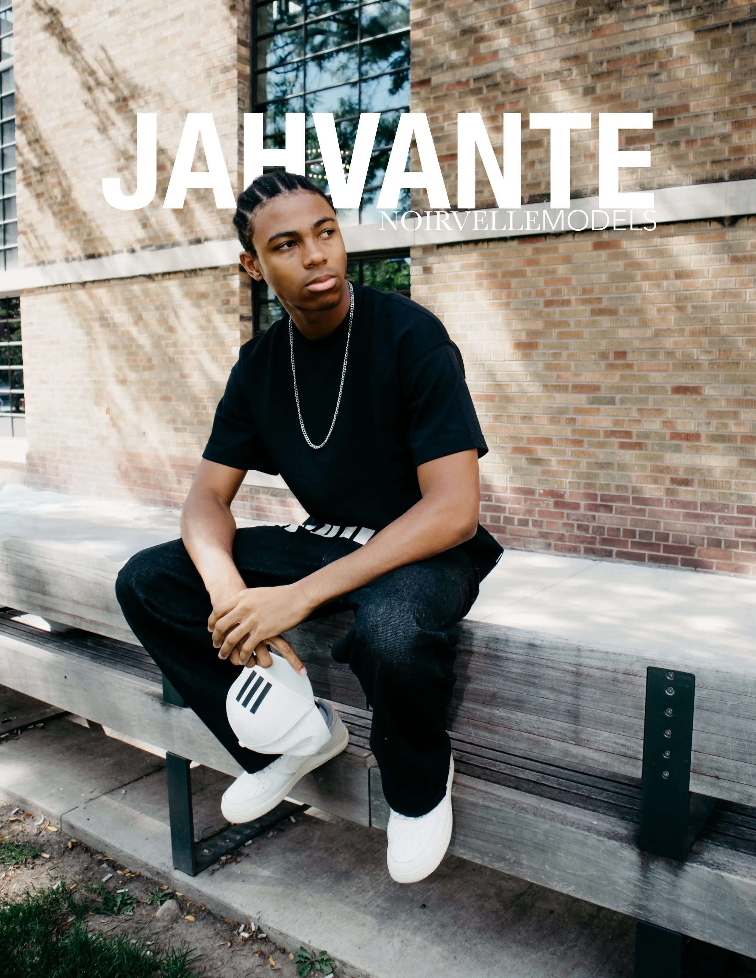 Jahvante, male fashion model represented by Noirvelle Models, seated outdoors on a bench in a black outfit.