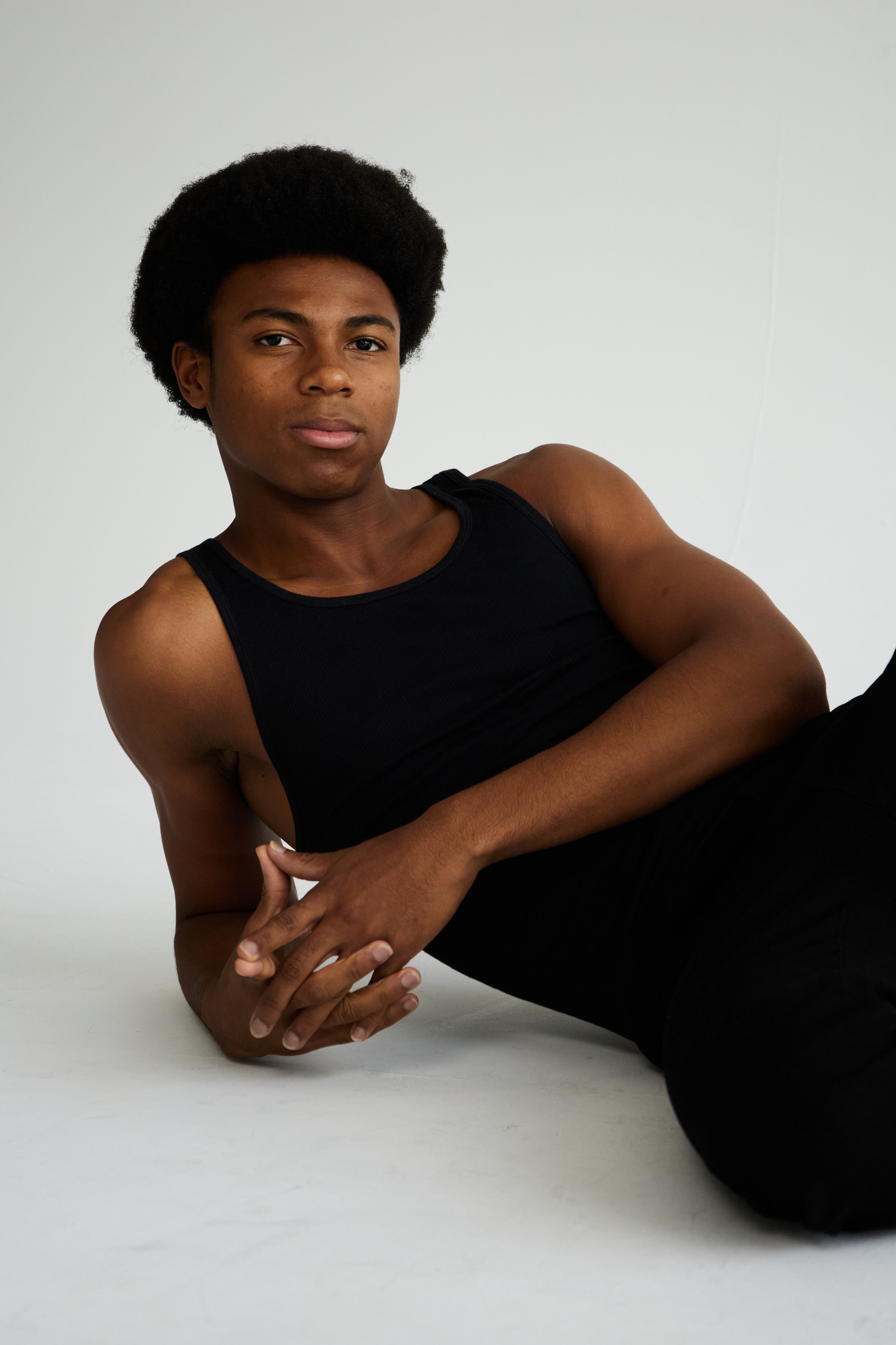  Jahvante, male fashion model represented by Noirvelle Models, posing in a black sleeveless top against a white studio background.

