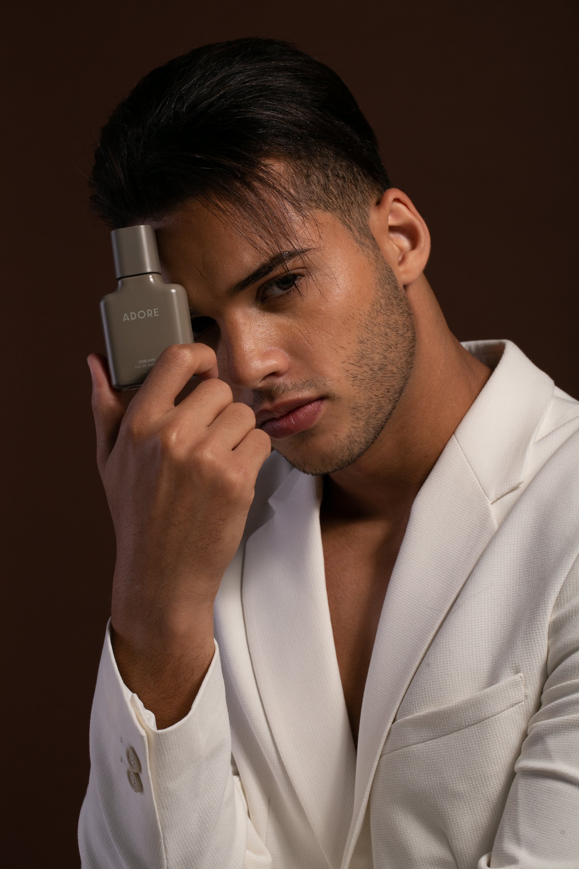 Bashir, male fashion model represented by Noirvelle Models, wearing a white blazer and posing with a fragrance bottle in a commercial campaign.
