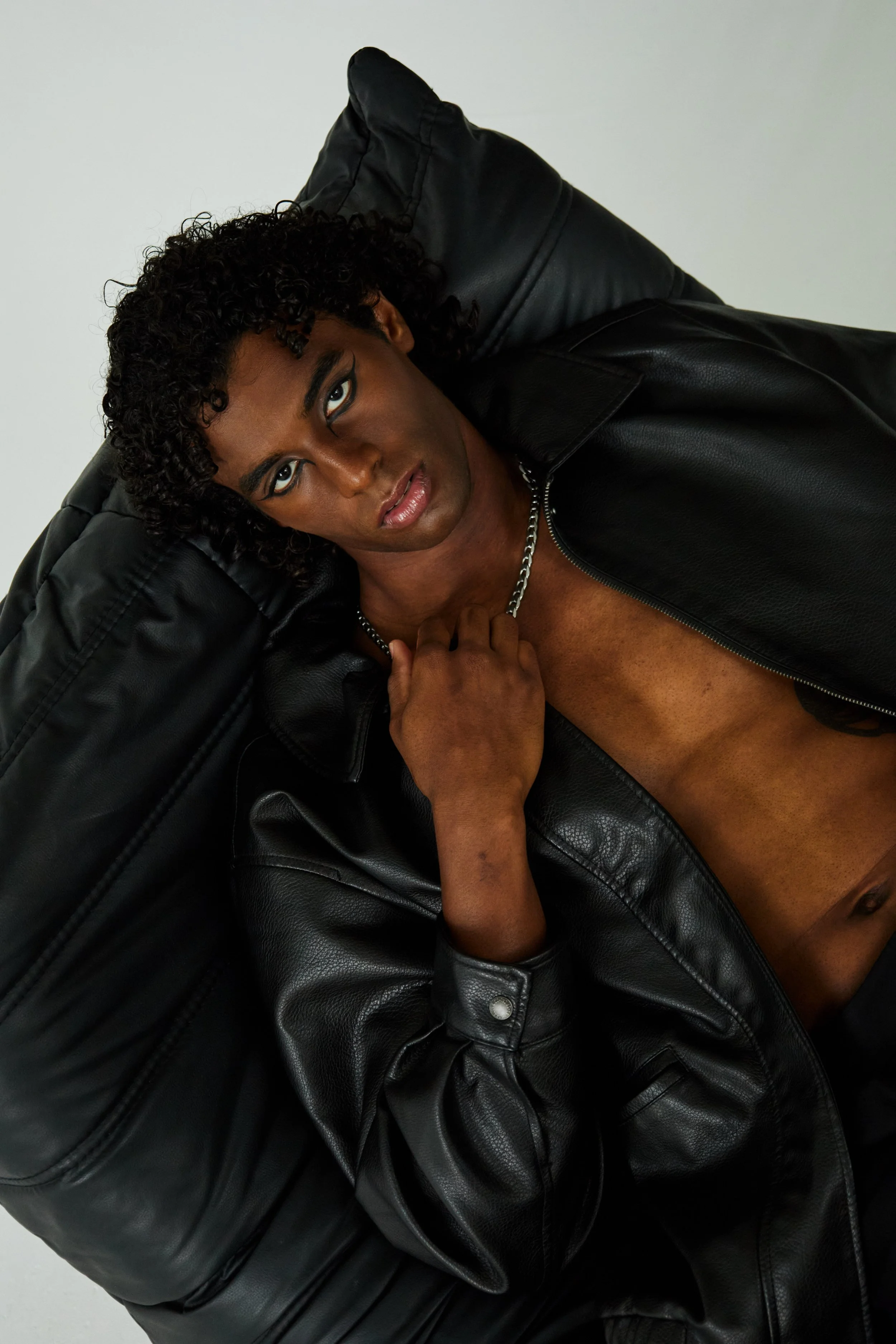  Xander, male fashion model represented by Noirvelle Models, wearing a black leather jacket in a dark editorial portrait.
