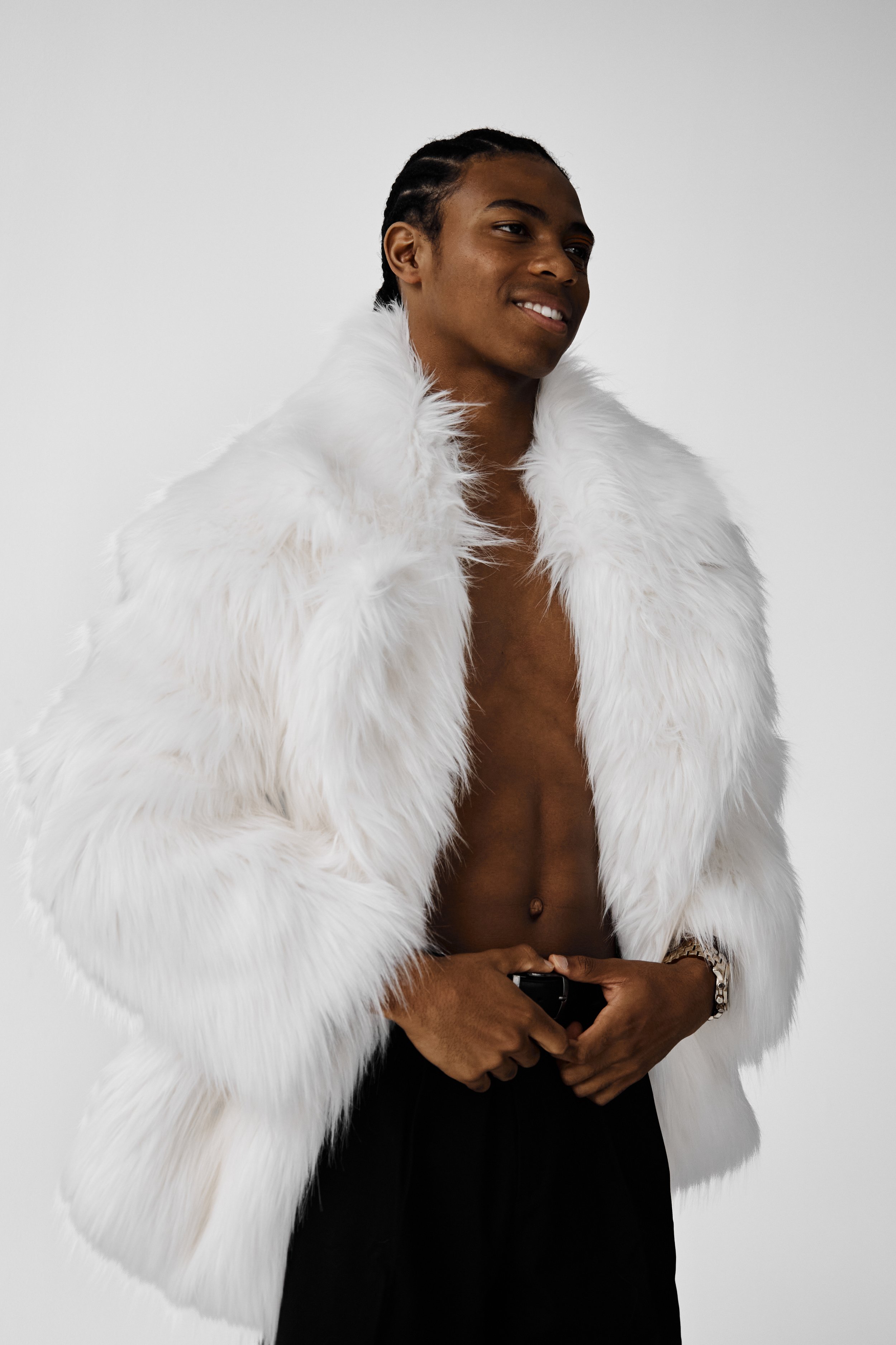 Jahvante, male fashion model represented by Noirvelle Models, posing in a white fur coat against a white studio background.
