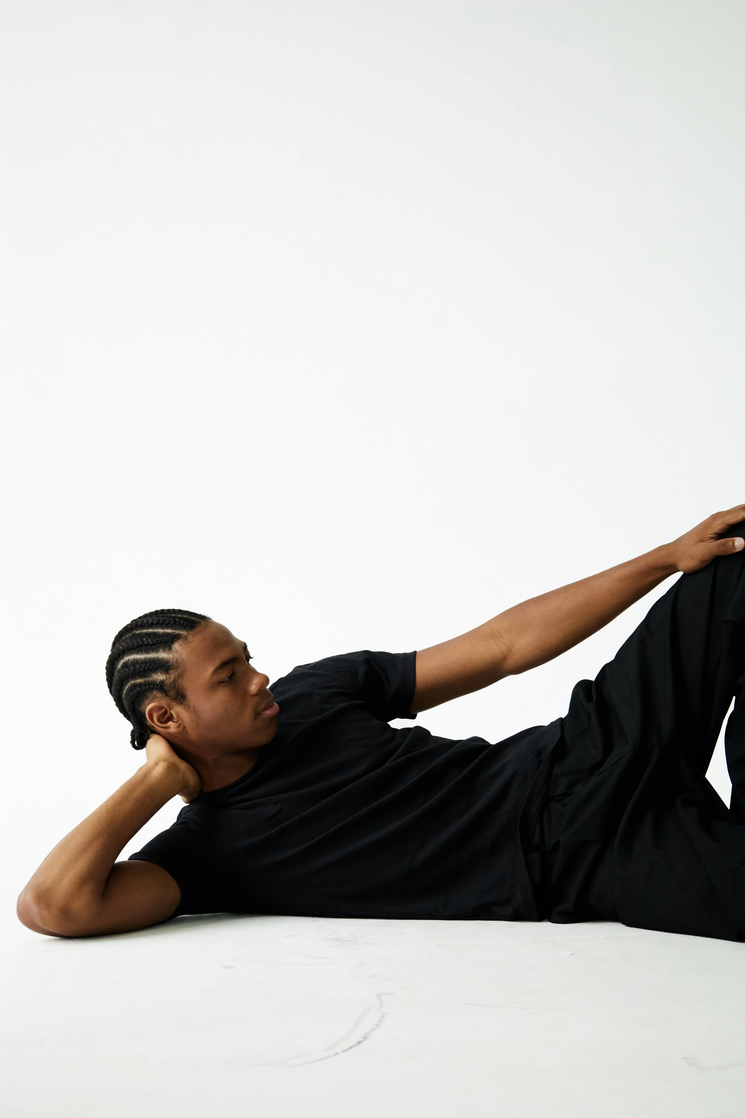 Jahvante, male fashion model represented by Noirvelle Models, posing on the floor in black clothing against a white studio background.

