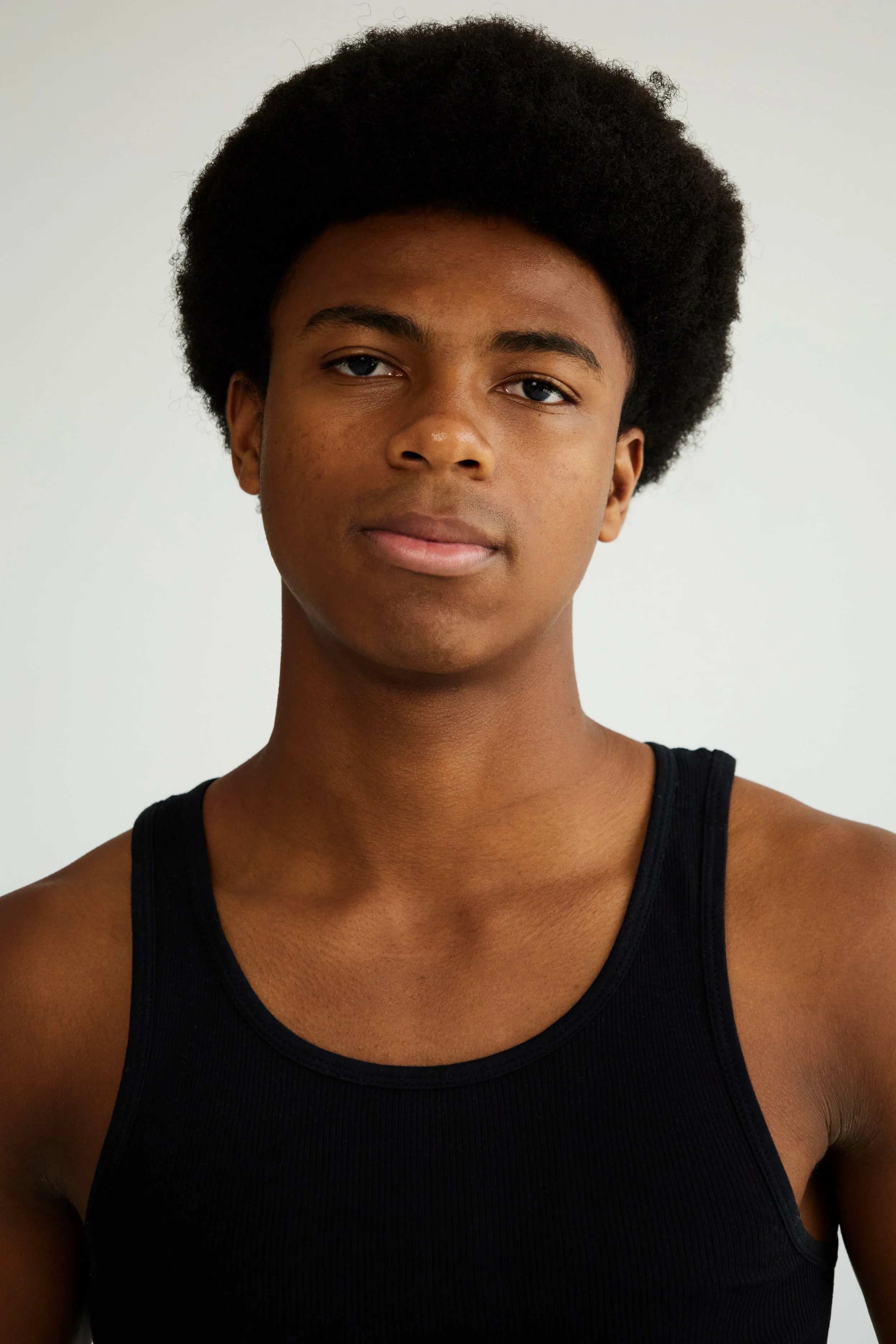 Jahvante, male fashion model represented by Noirvelle Models, close-up portrait in a black tank top against a white studio background.
