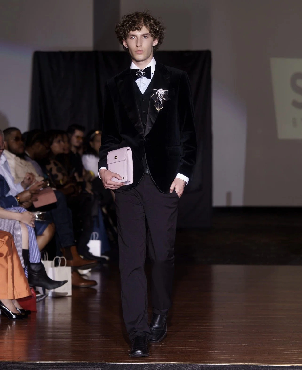  Andrea, male fashion model represented by Noirvelle Models, walking the runway in a black velvet blazer and black trousers during a fashion show.