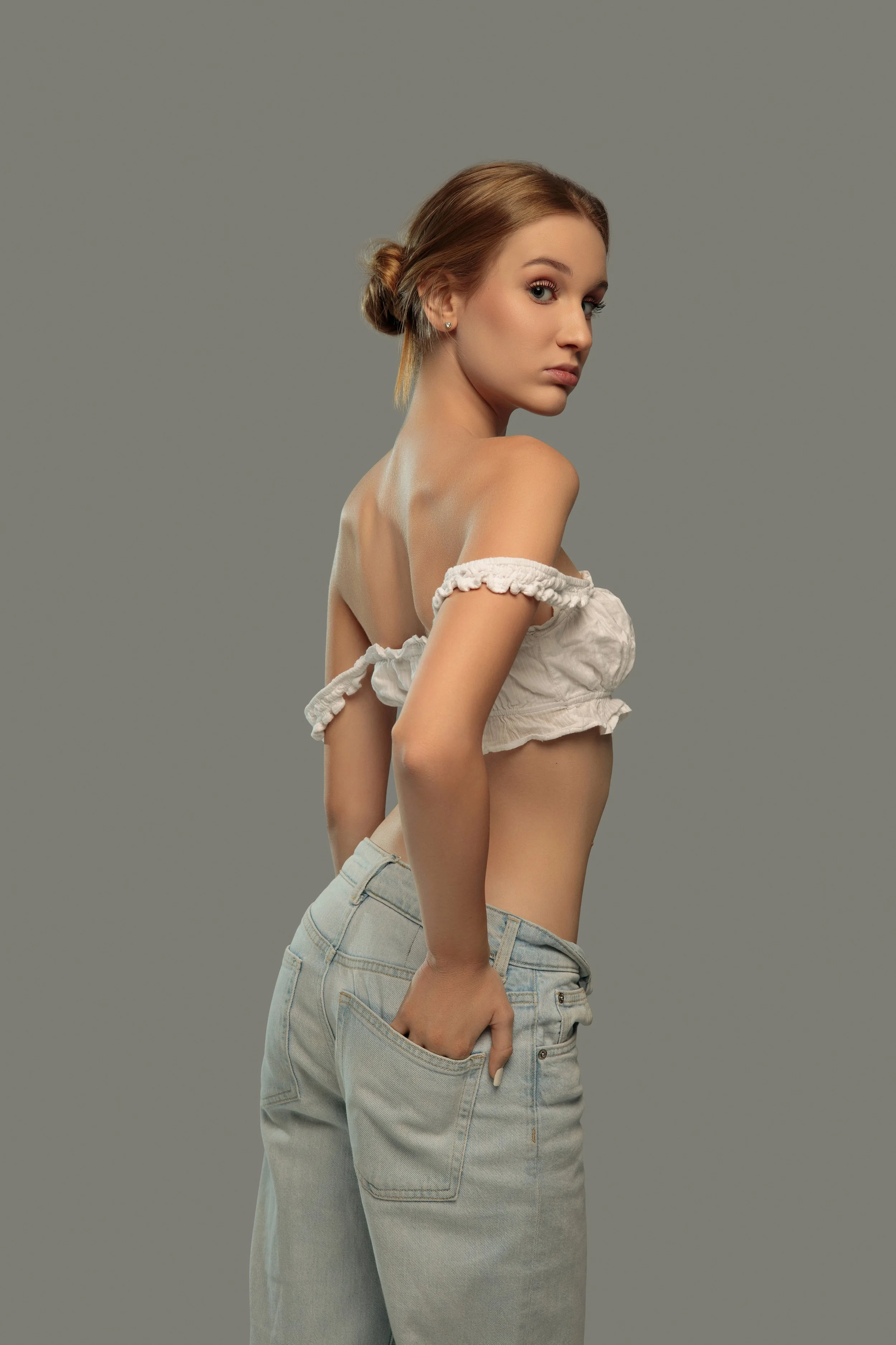 Victoria, female model represented by Noirvelle Models, posing in a light off-the-shoulder top and jeans for a fashion portrait.
