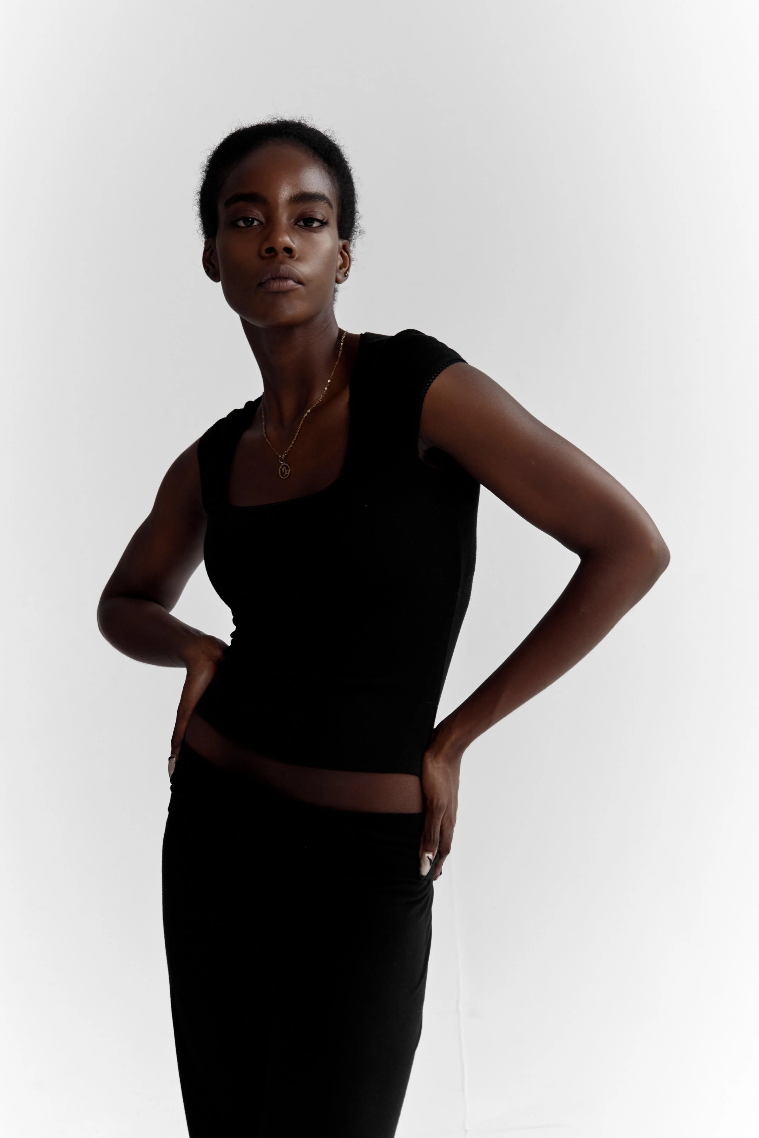 Daisy, female fashion model represented by Noirvelle Models, wearing a black sleeveless top and long black skirt in a studio portrait.

