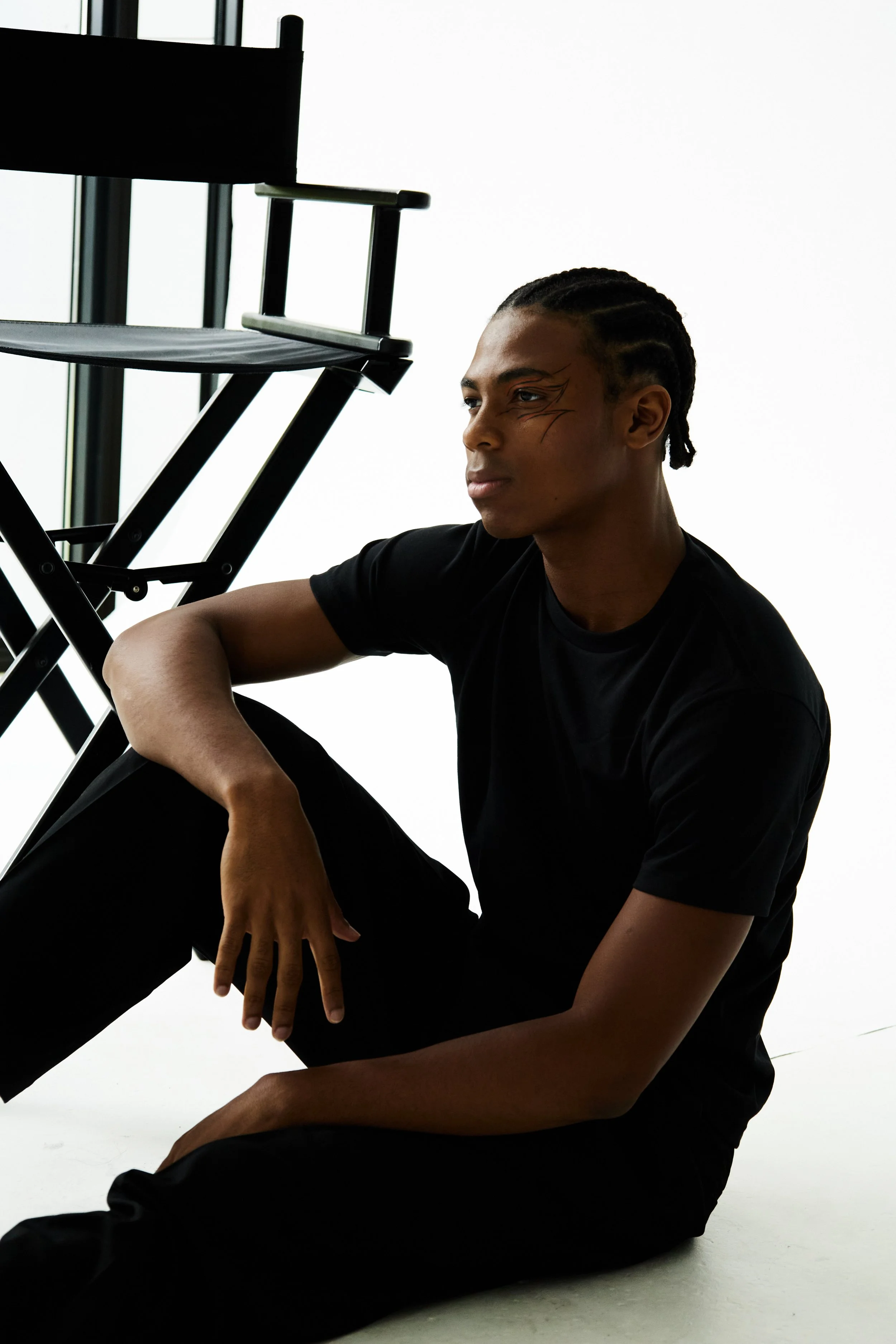 Jahvante, male fashion model represented by Noirvelle Models, seated on the floor in a fashion editorial studio portrait.
