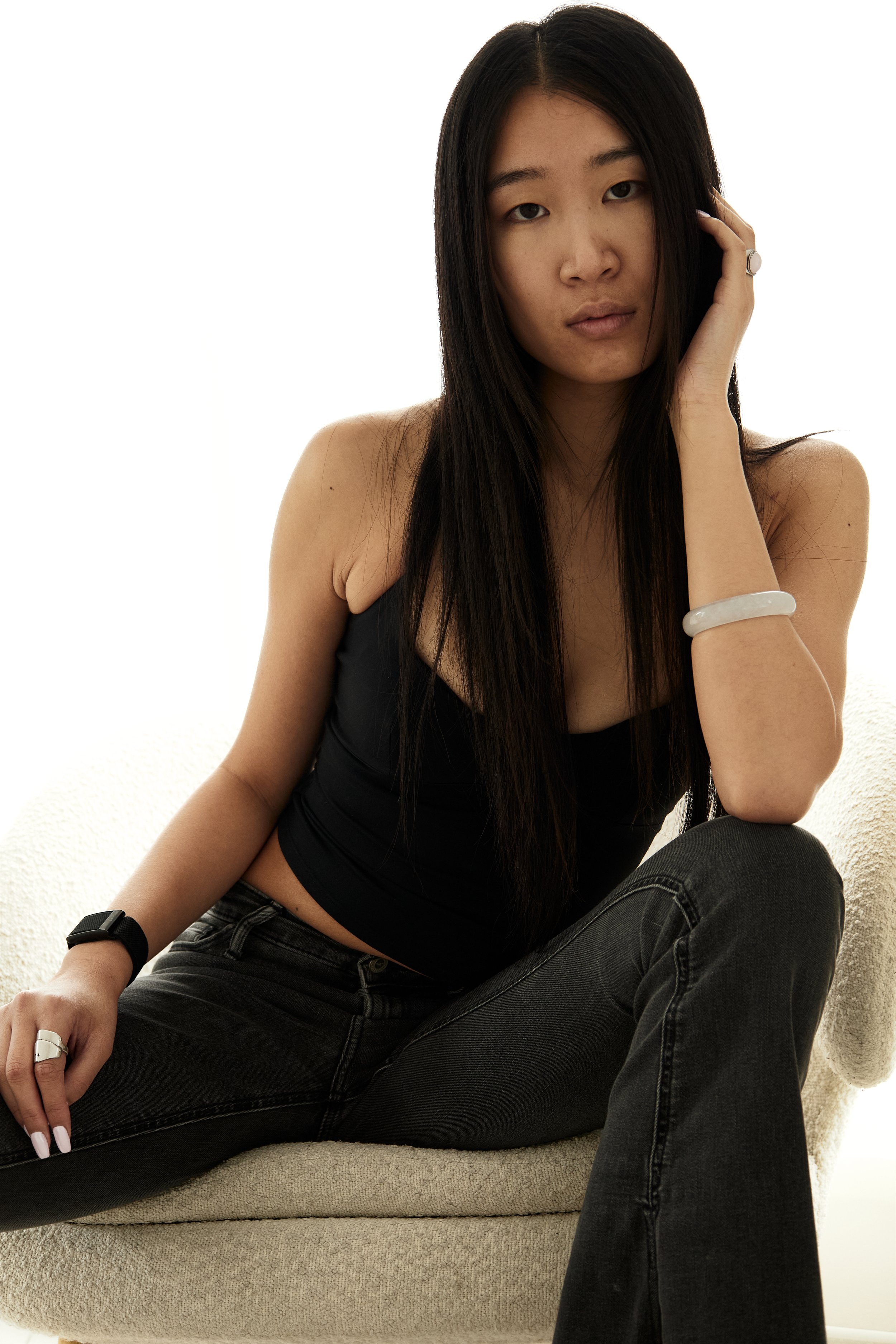 Jolin — female fashion model represented by Noirvelle Models, seated in a studio setting wearing a black outfit.