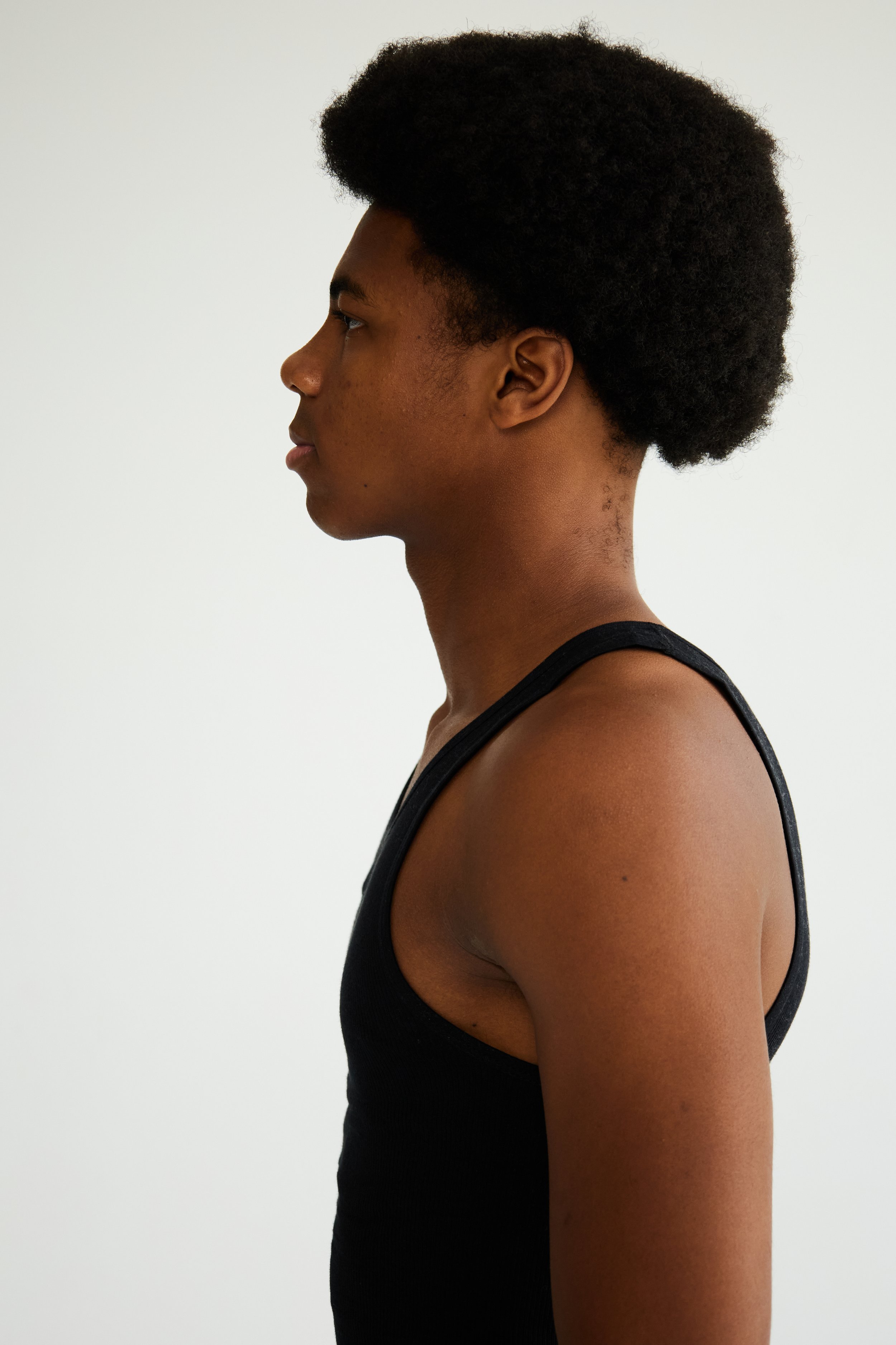 	
Jahvante, male fashion model represented by Noirvelle Models, side-profile portrait in a black sleeveless top against a white studio background.