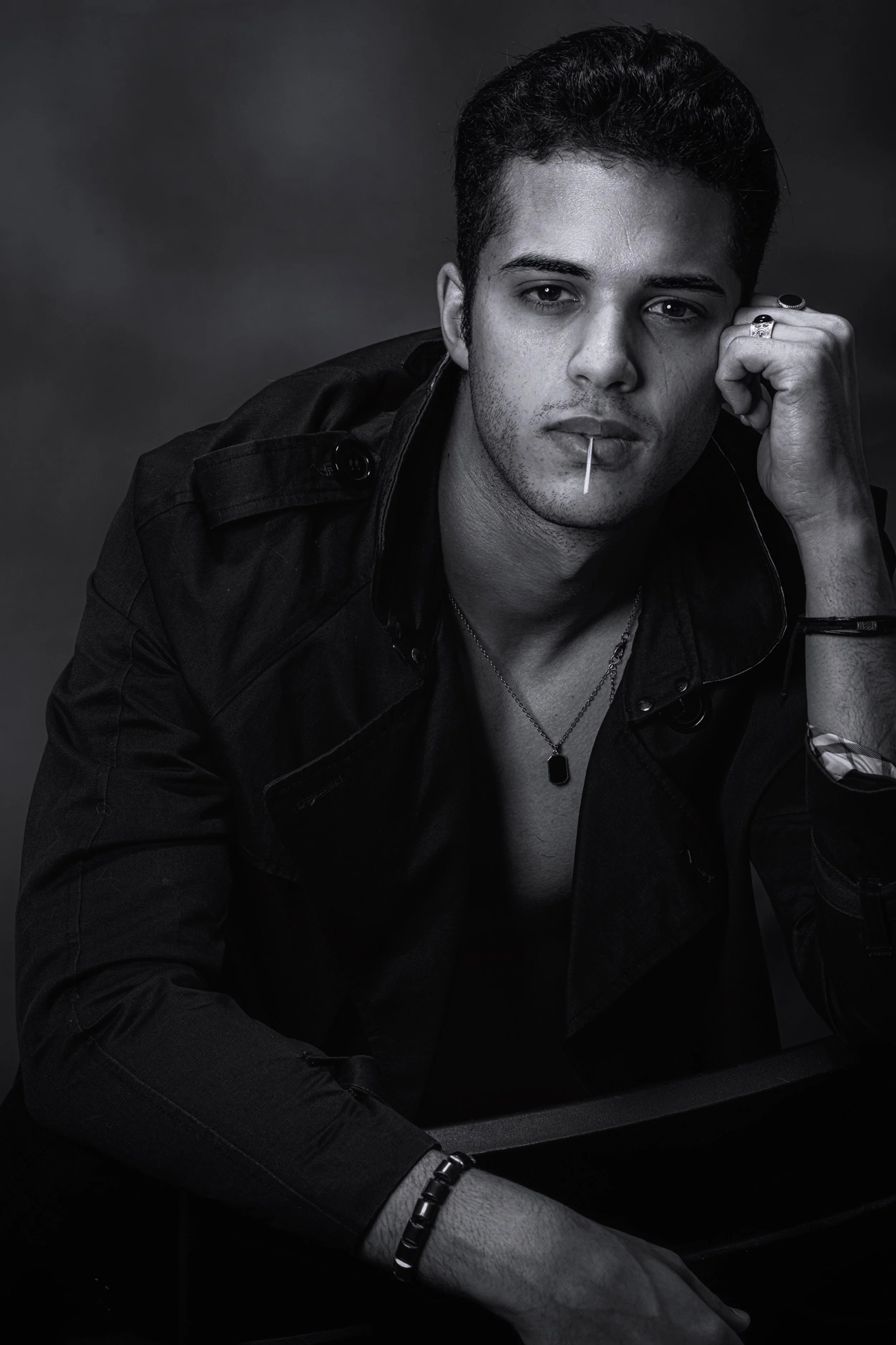 Bashir, male fashion model represented by Noirvelle Models, in a black and white editorial portrait wearing a dark jacket and jewelry.
