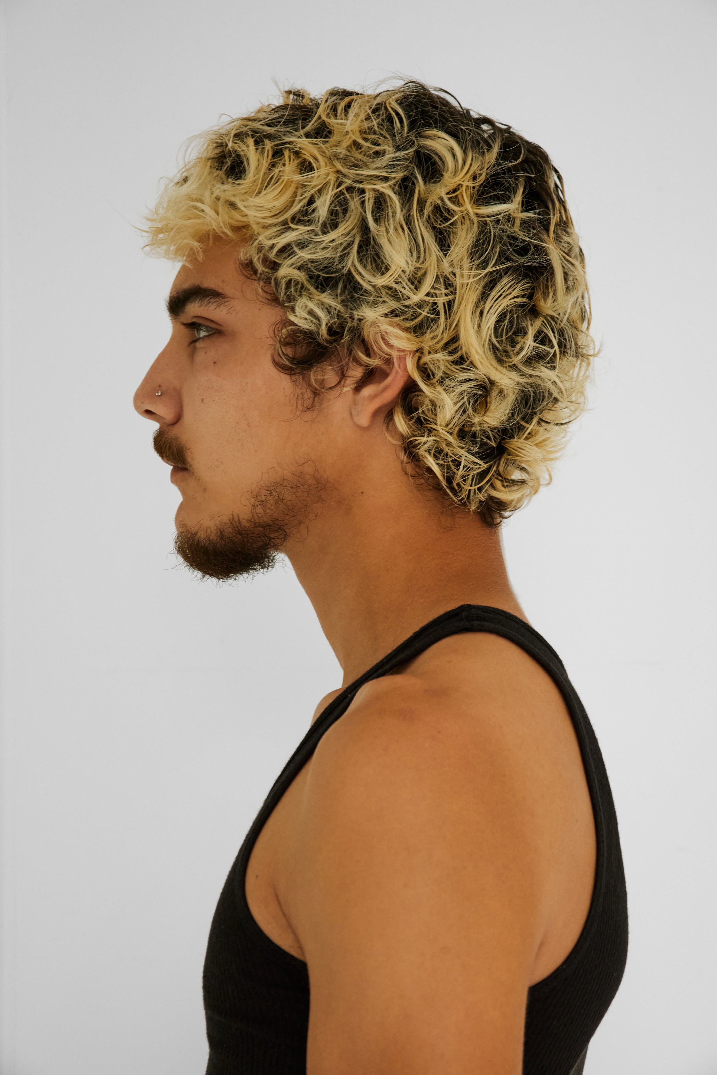  Quinton, male fashion model represented by Noirvelle Models, side profile in a black tank top against a white studio background.
