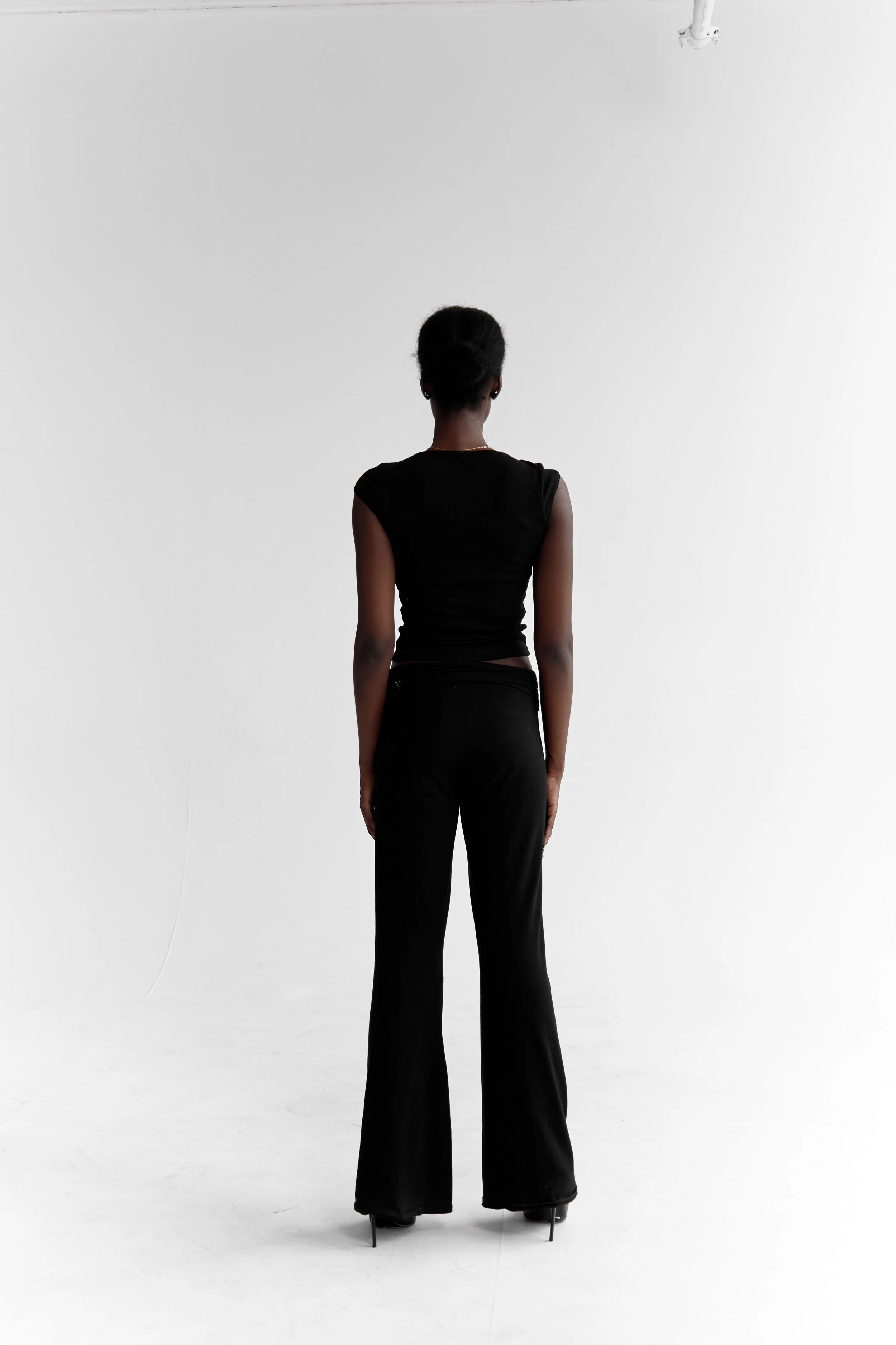 Daisy, female fashion model represented by Noirvelle Models, standing in an all-black look against a white studio background.
