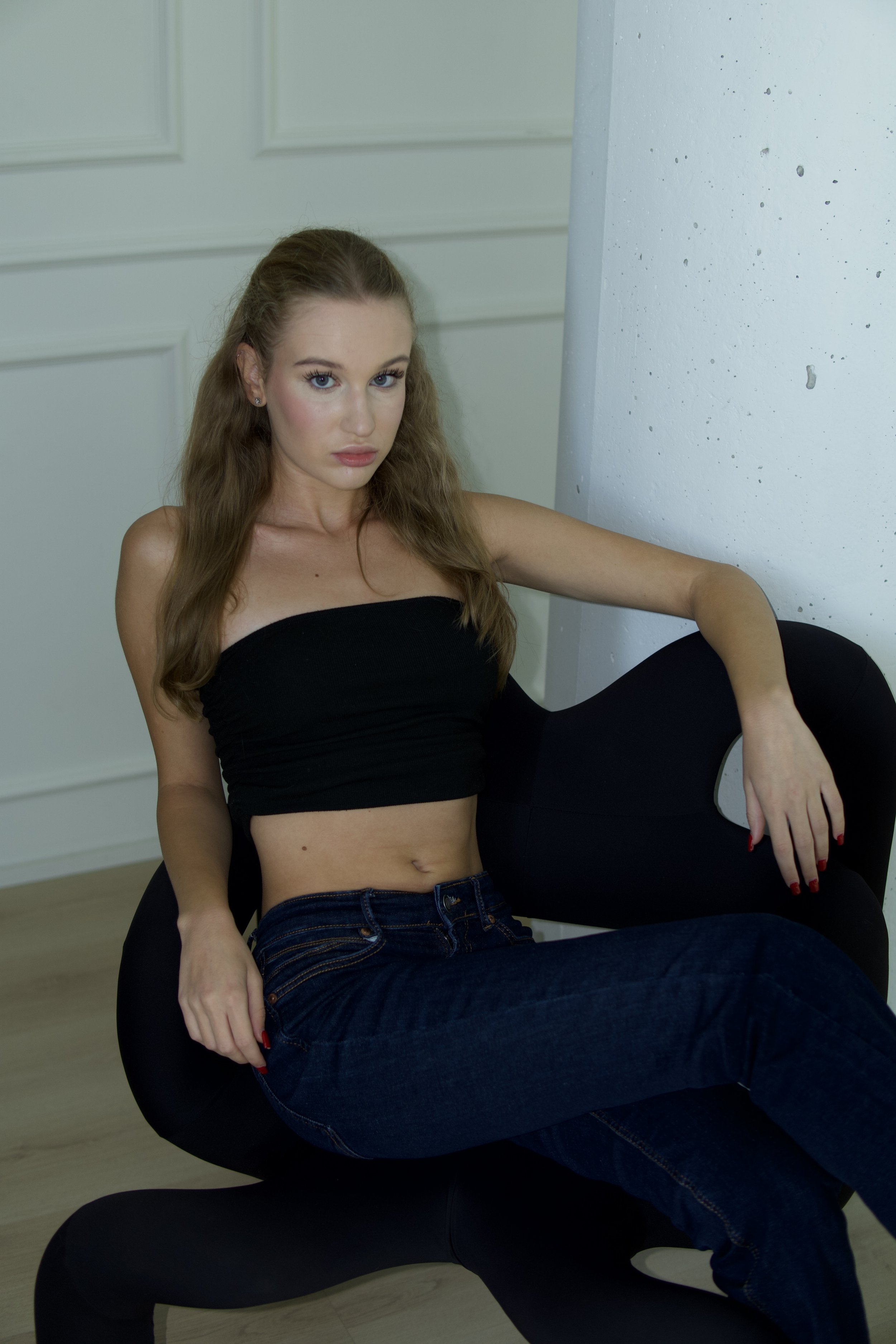  Victoria, female model represented by Noirvelle Models, seated in a black top and jeans during a minimalist fashion portrait.
