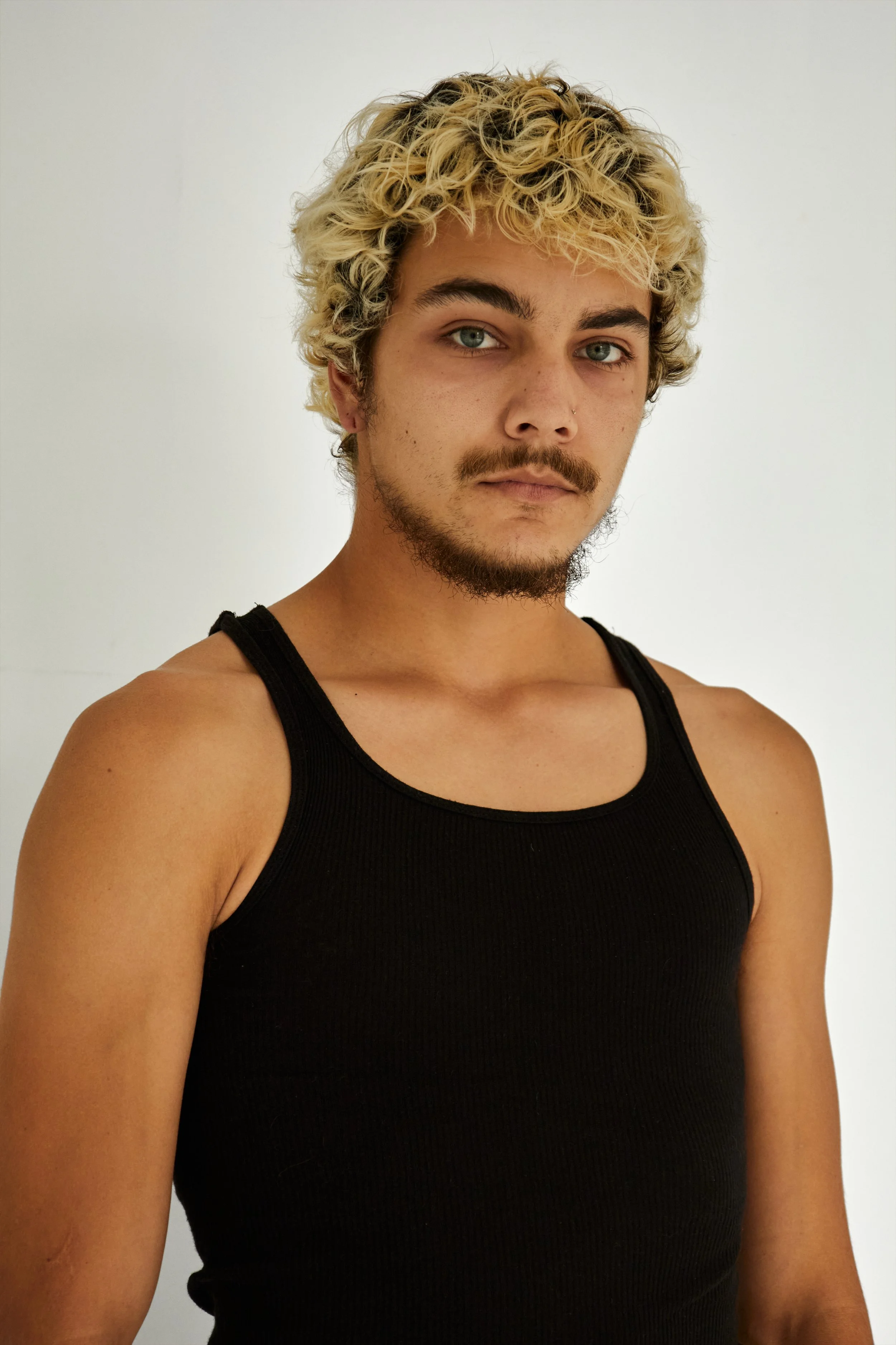 Quinton, male fashion model represented by Noirvelle Models, portrait in a black tank top against a white studio background.

