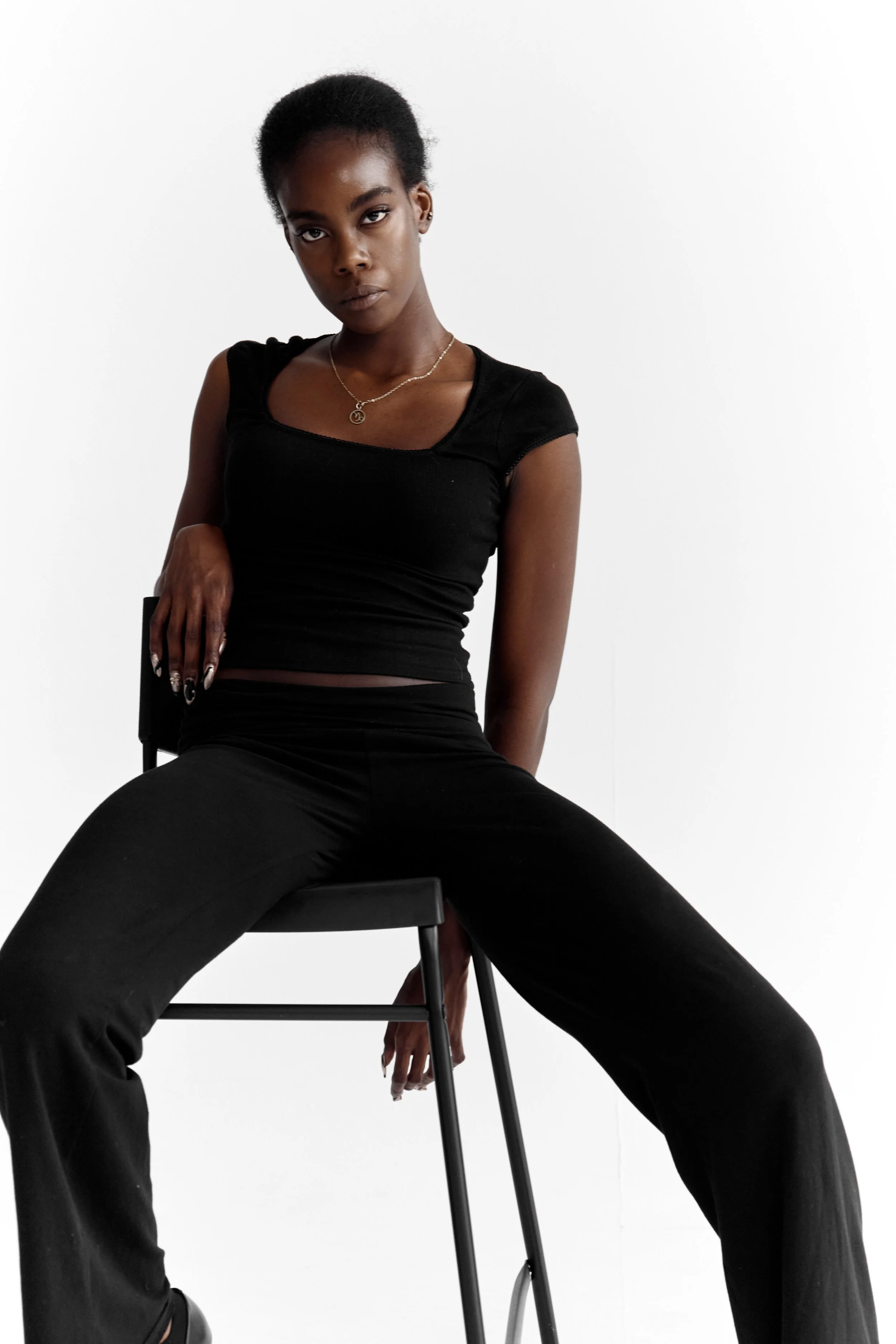 Daisy, female fashion model represented by Noirvelle Models, posing seated in an all-black look against a white studio background.
