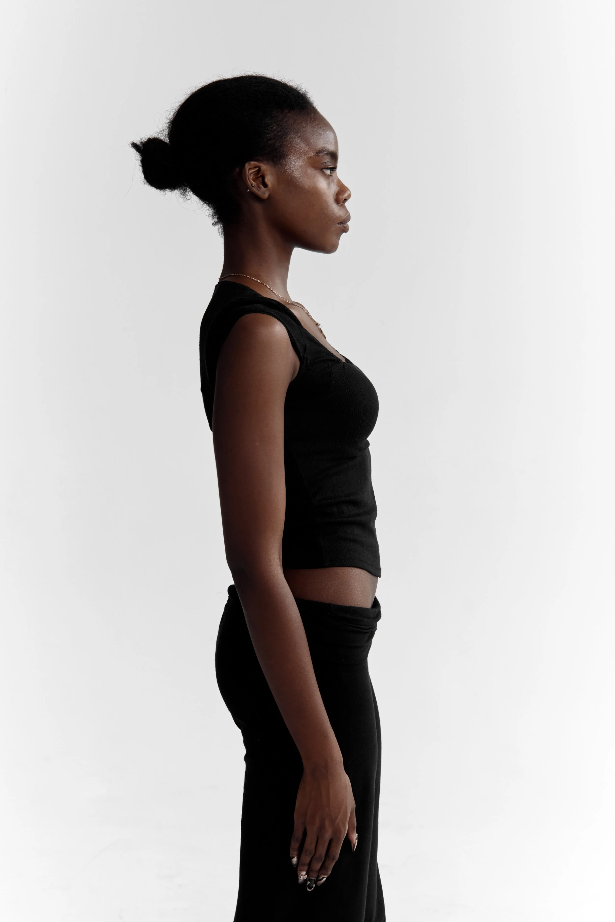 Daisy, female fashion model represented by Noirvelle Models, standing in profile in an all-black look against a white studio background.