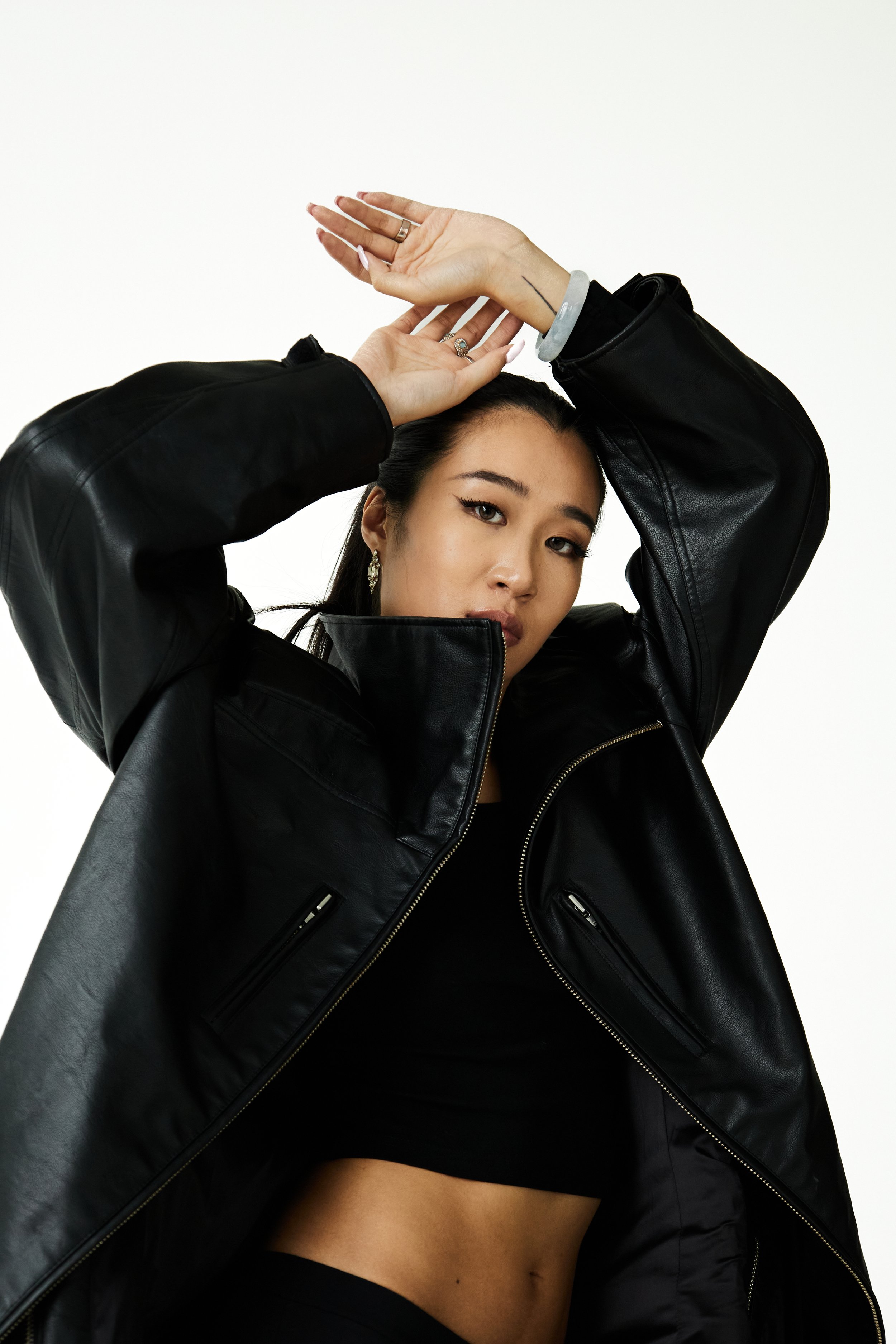 Joline, female fashion model represented by Noirvelle Models, posing in a black leather jacket and crop top against a white studio background.

