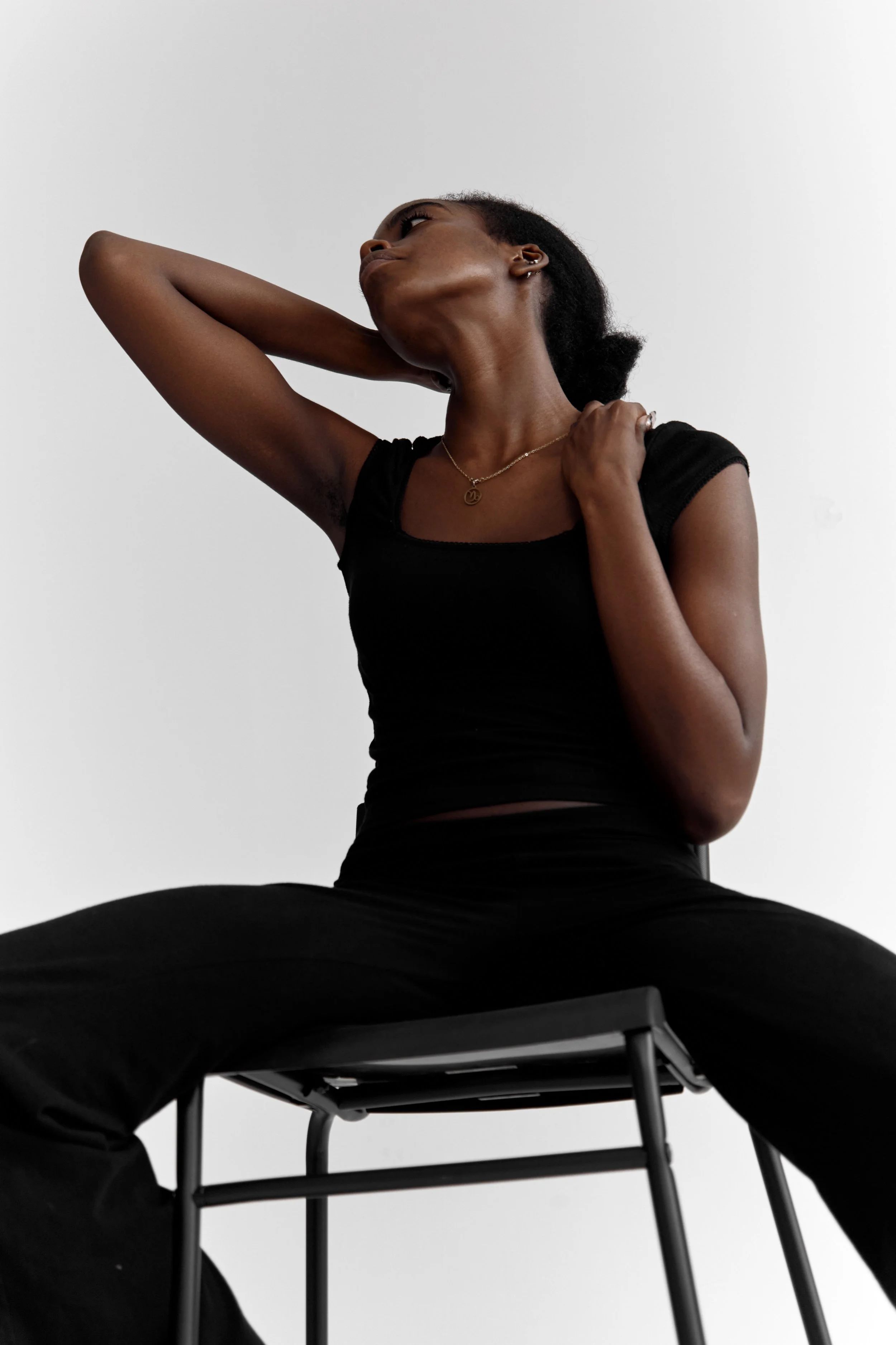 Daisy, female fashion model represented by Noirvelle Models, posing seated in a black outfit against a white studio background.