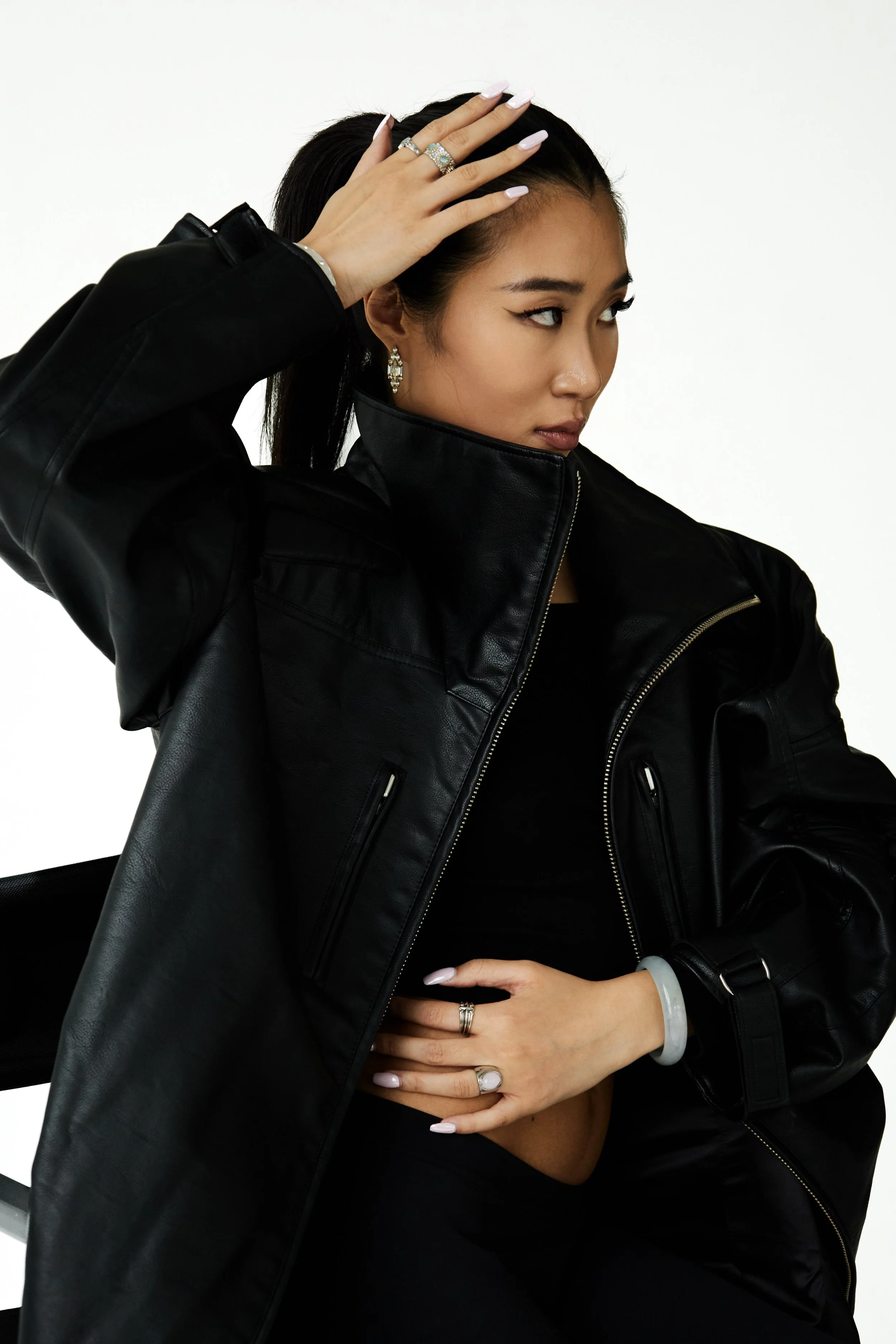 Joline, female fashion model represented by Noirvelle Models, posing in a black leather jacket with statement jewelry against a white studio background.

