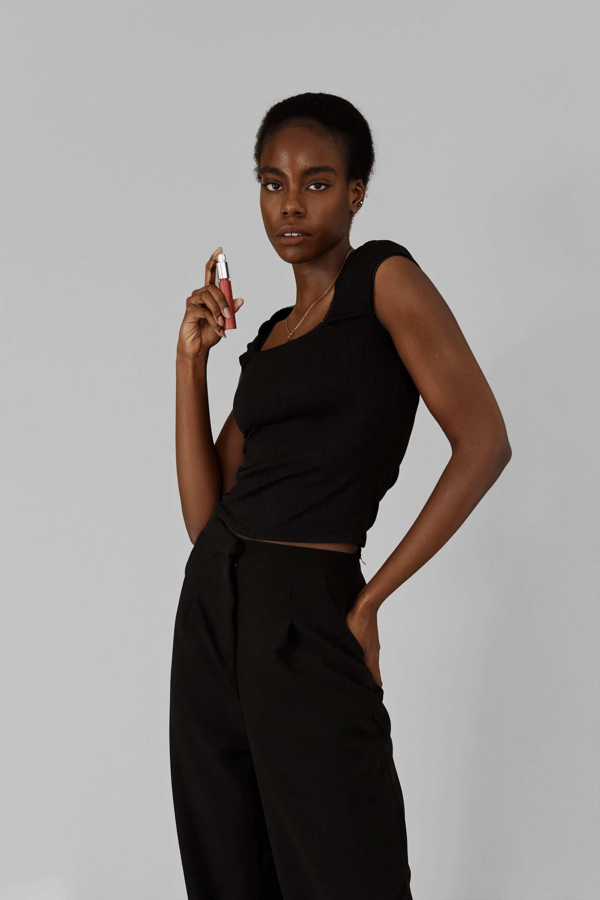  Daisy, female fashion model represented by Noirvelle Models, standing in a black sleeveless look against a grey studio background.
