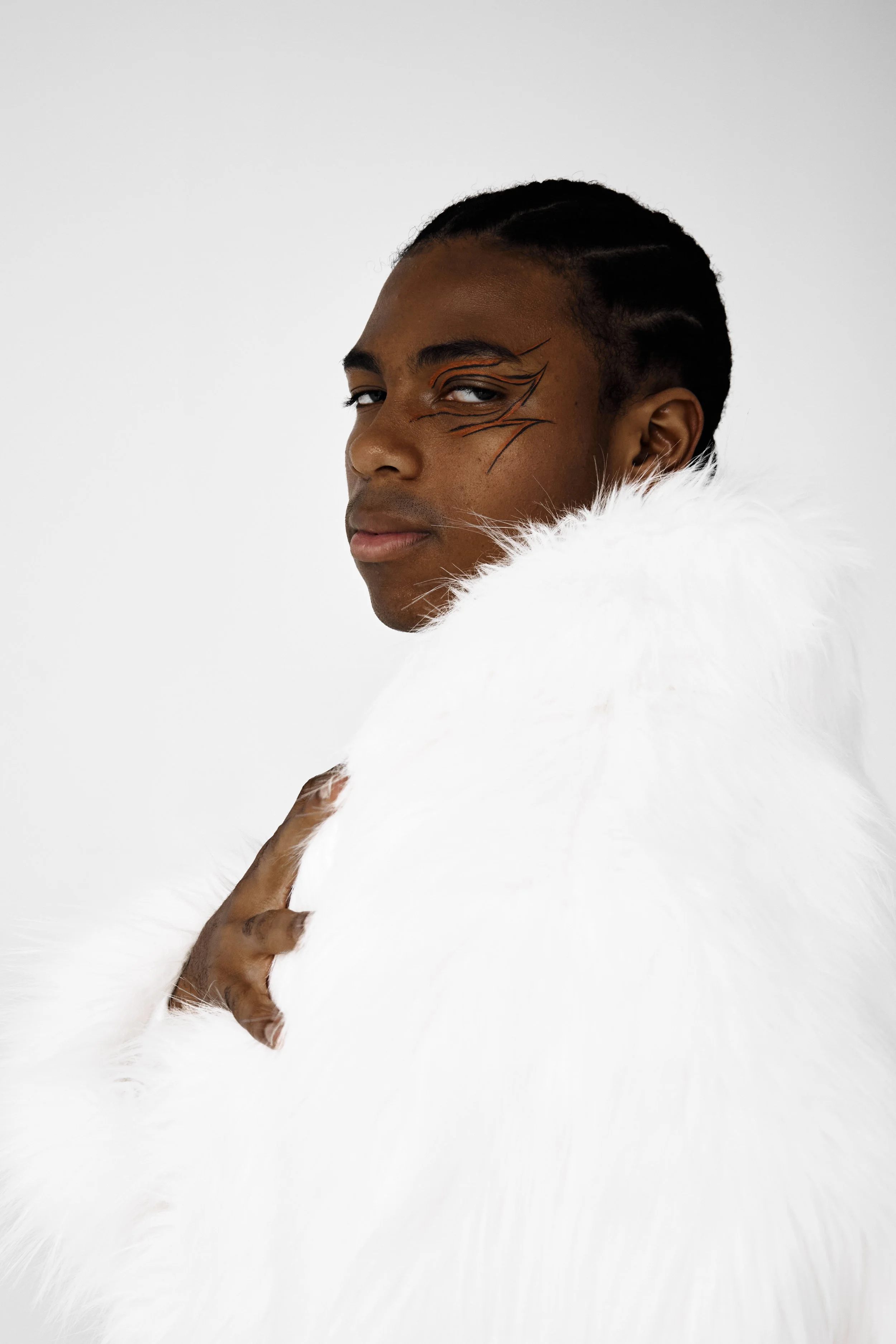 Jahvante, male fashion model represented by Noirvelle Models, editorial portrait wearing a white faux fur look against a light studio background.
