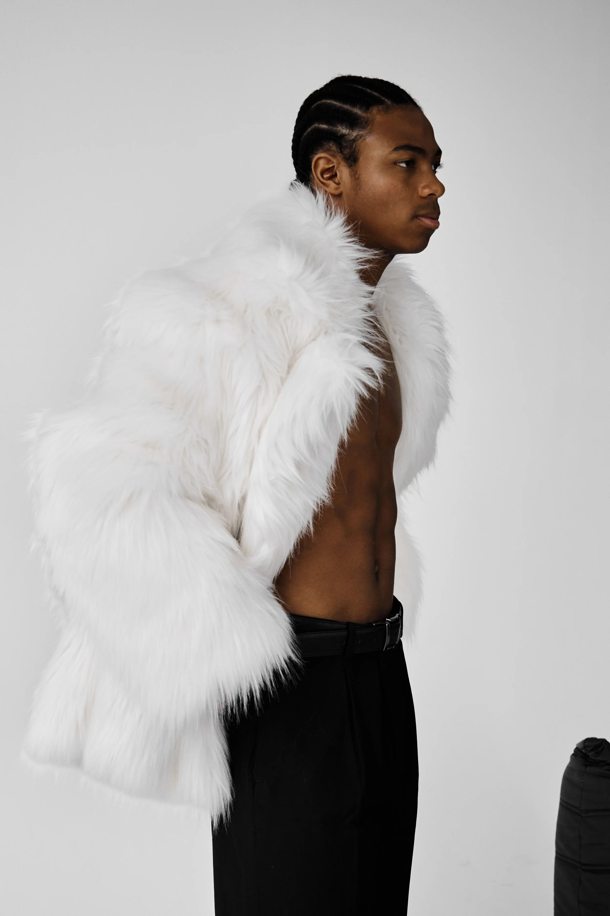 Jahvante, male fashion model represented by Noirvelle Models, posing in a white fur coat and black pants against a white studio background.
