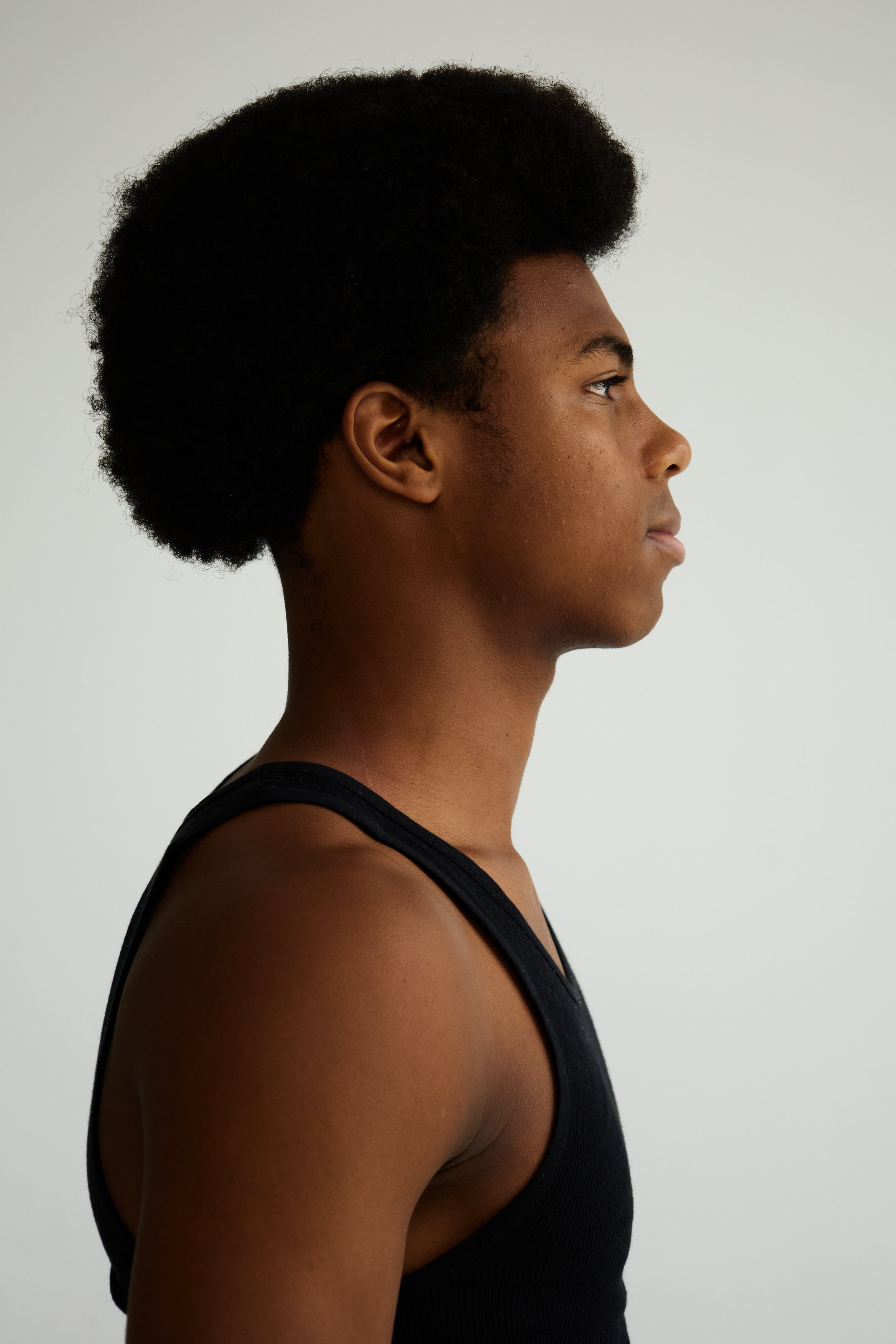 Jahvante, male fashion model represented by Noirvelle Models, side-profile portrait in a black sleeveless top against a white studio background.

