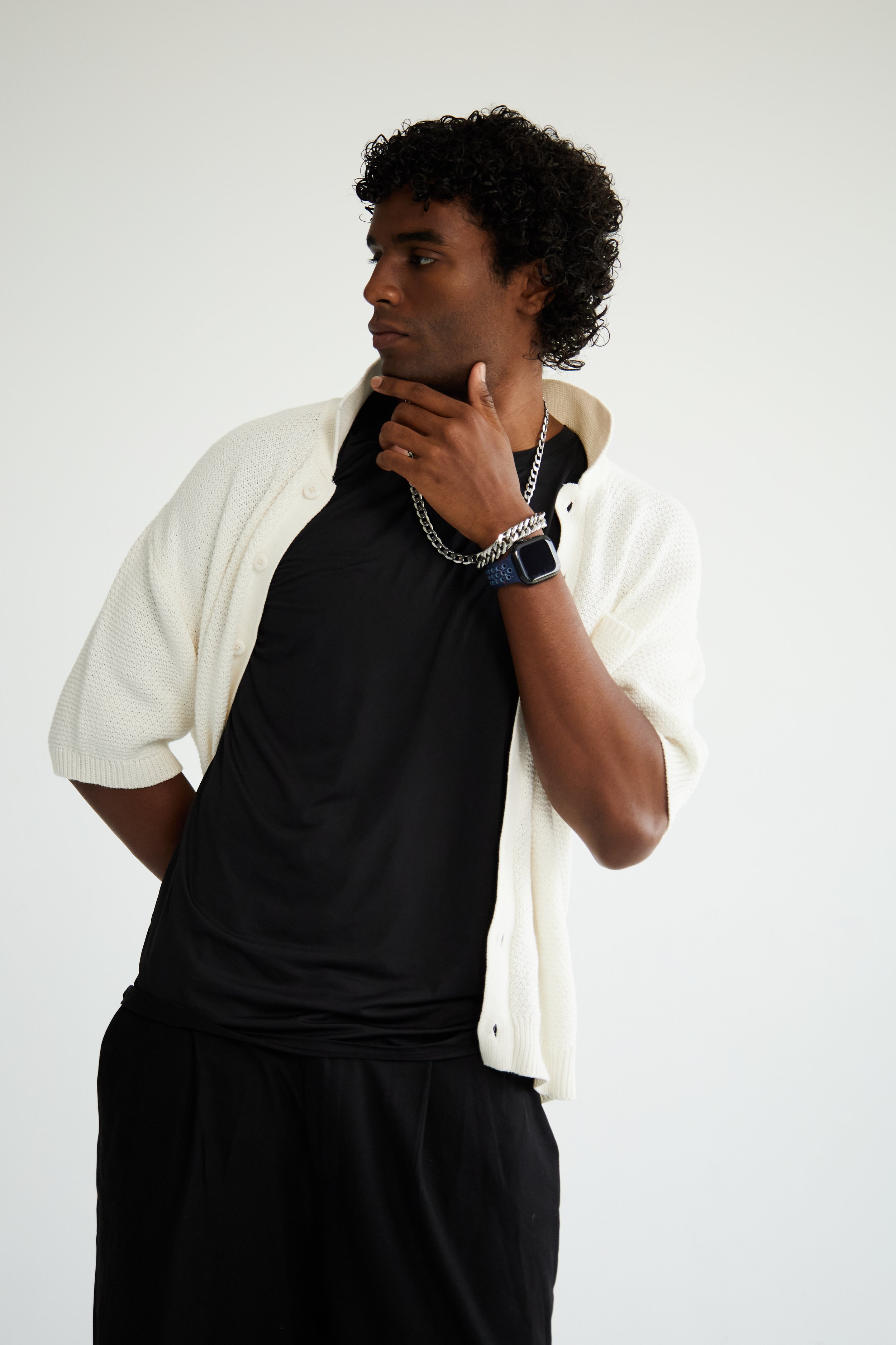 Xander, male fashion model represented by Noirvelle Models, wearing a black shirt and white cardigan in a studio portrait.
