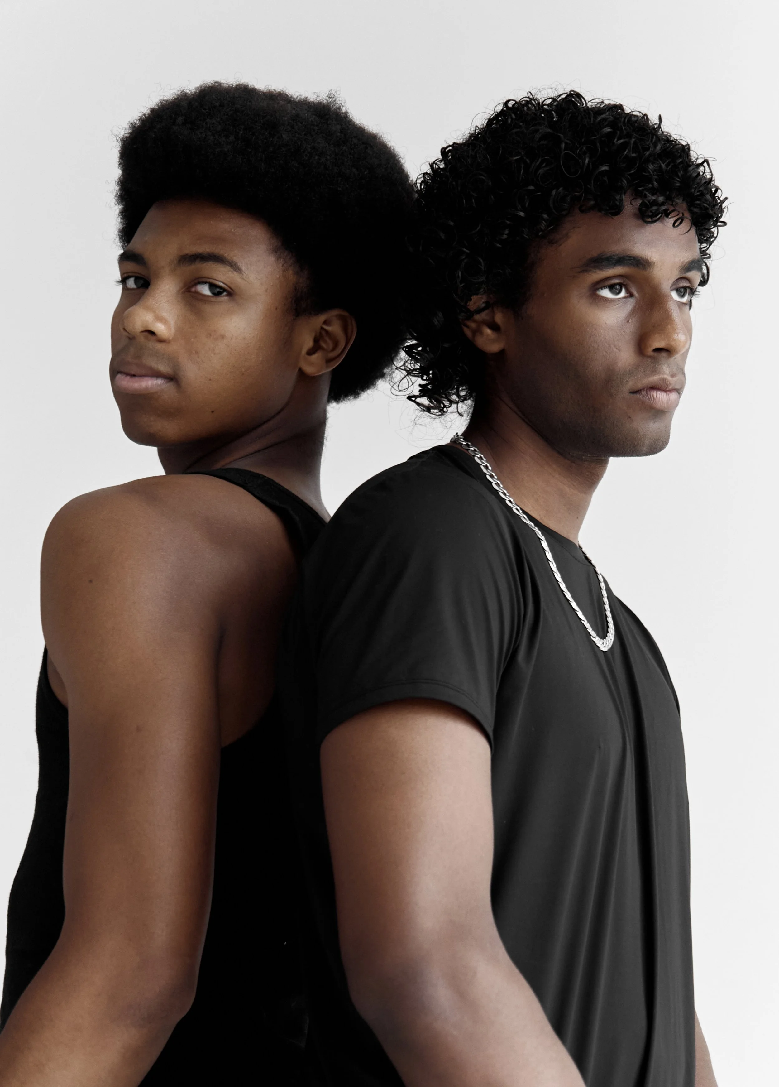Xander, male fashion model represented by Noirvelle Models, posing back-to-back with another male model in an all-black studio look.

