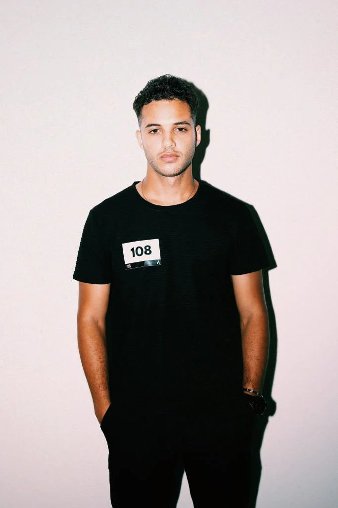 . Bashir, male fashion model represented by Noirvelle Models, photographed in a black T-shirt against a clean white studio background.
