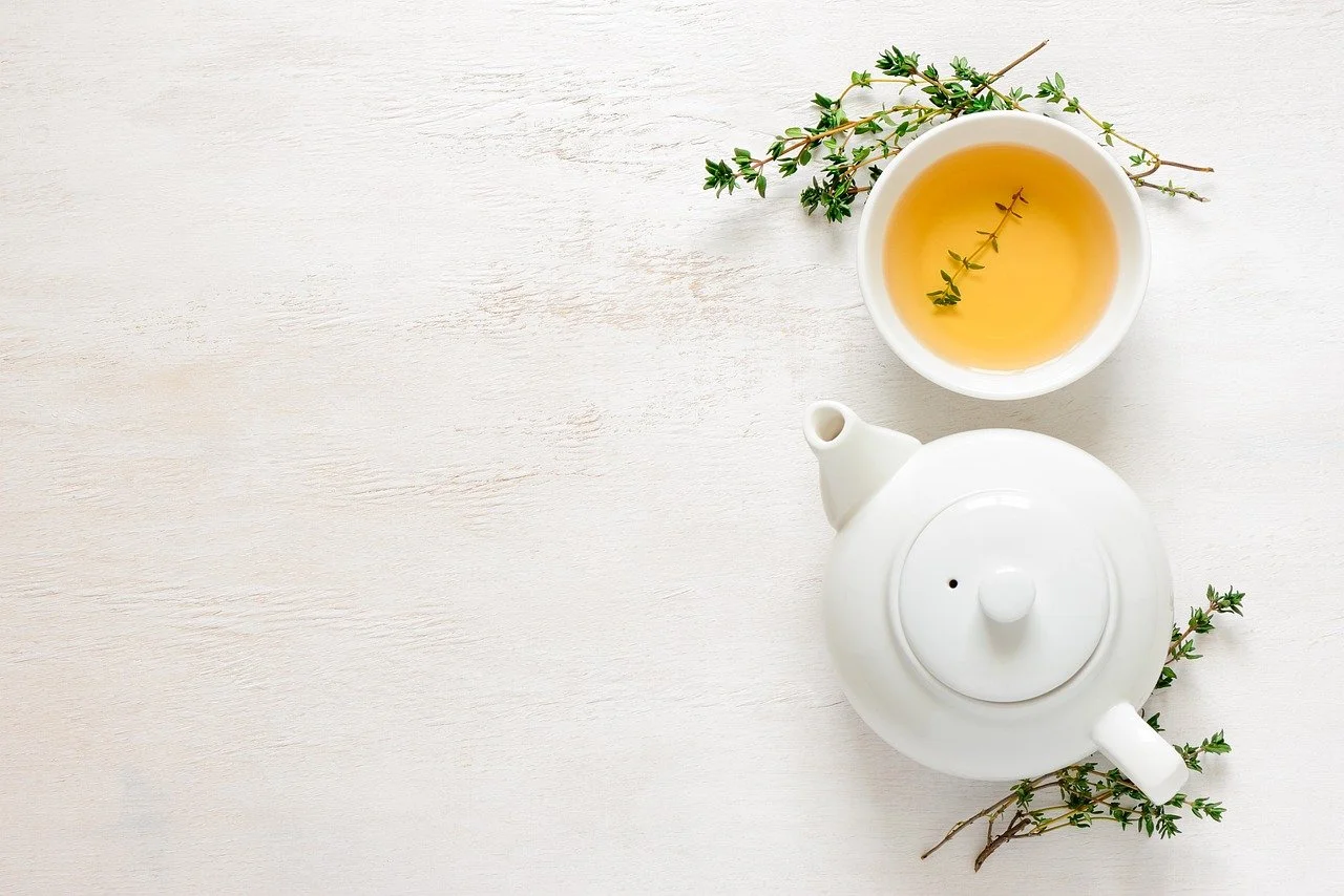White teapot and cup of herbal tea with fresh thyme on a cream painted wood surface.