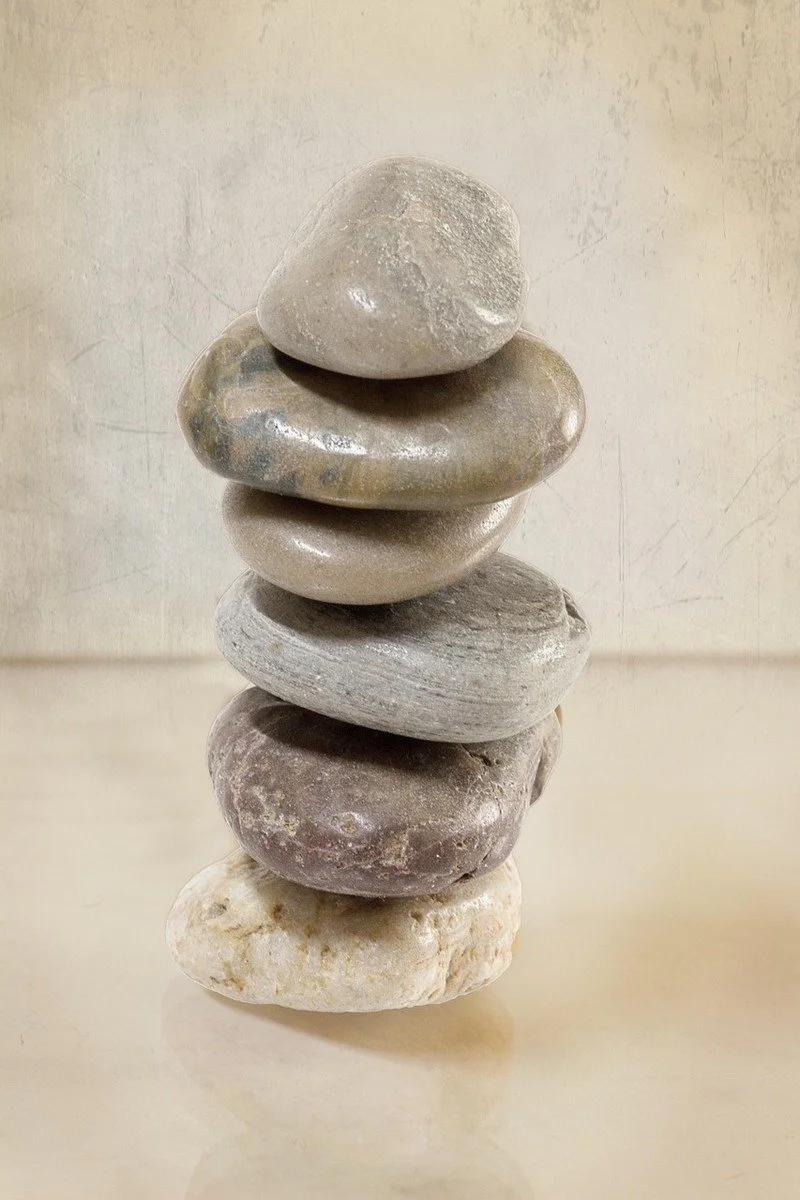 Smooth grey and sand-coloured stones balanced in a calm stack against a soft beige background.