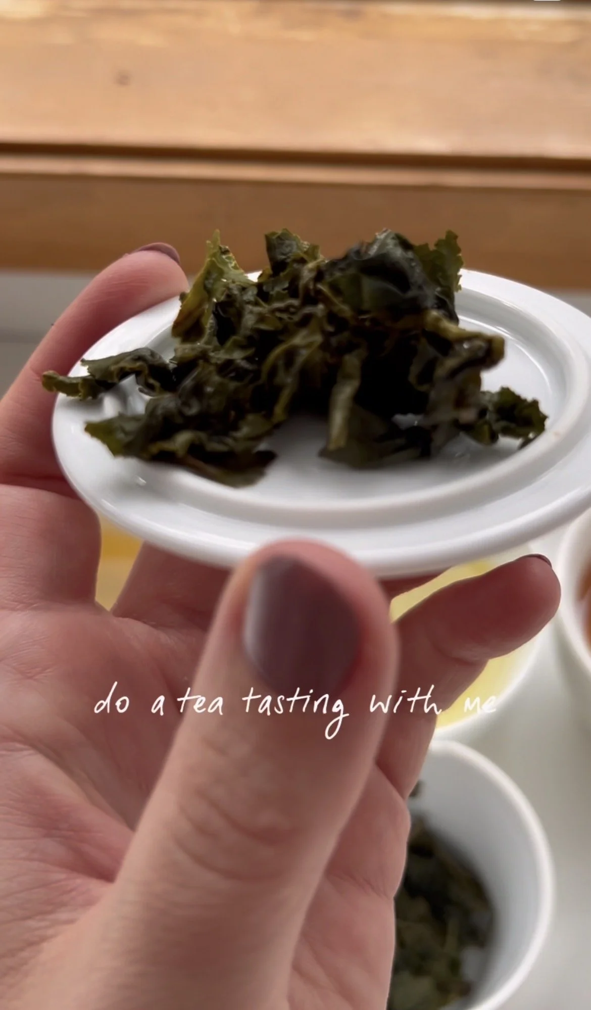 Close‑up of a hand holding a small white dish with dried seaweed during a tea tasting ritual. Other tasting dishes are visible in the background. Text overlay reads “do a tea tasting with me.” Perfect for tea education, sensory analysis, and mindful.