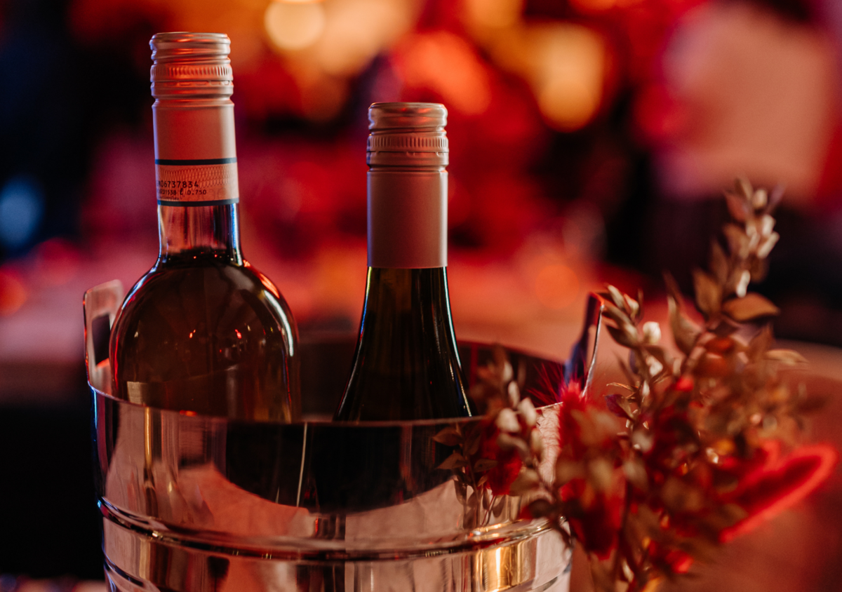 Two bottles of wine in an ice bucket with decorative flowers on the side, illuminated by warm, festive lighting.