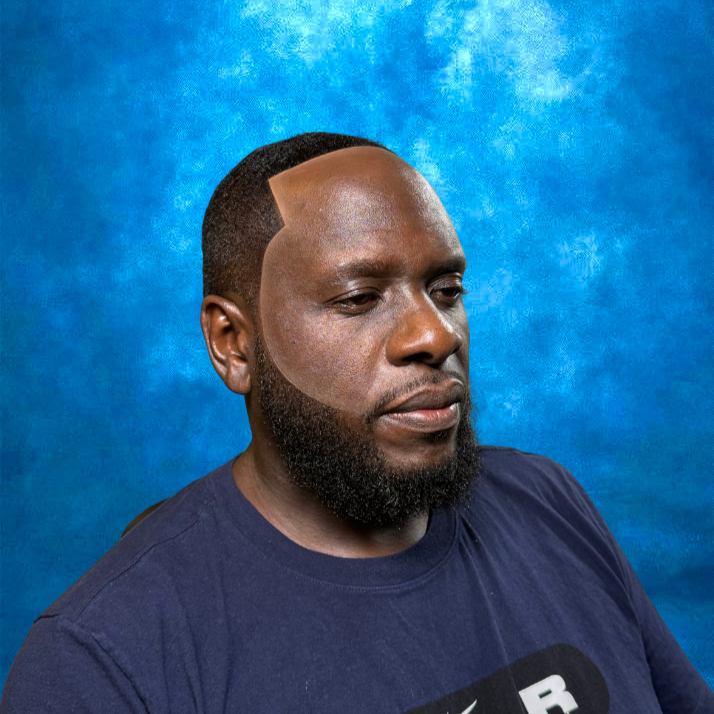 A man with a beard and short hair, wearing a navy blue shirt, against a blue textured background.