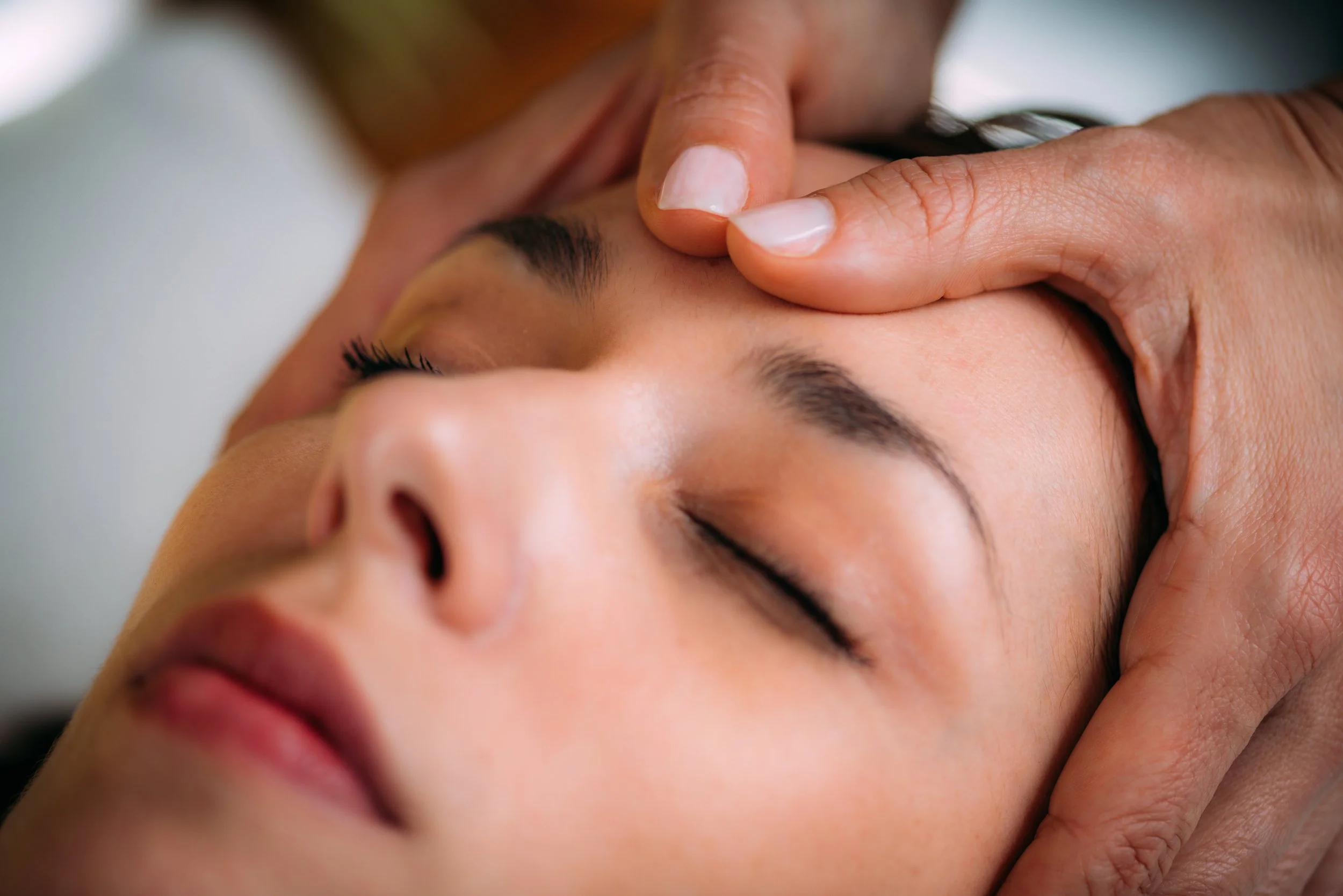 A person receiving craniosacral therapy with closed eyes, lying down, showing a relaxing facial treatment.