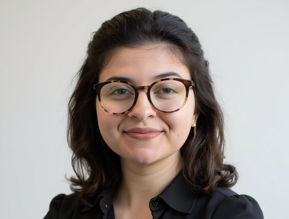 A woman with dark brown hair wearing glasses smiling at the camera against a plain white background.