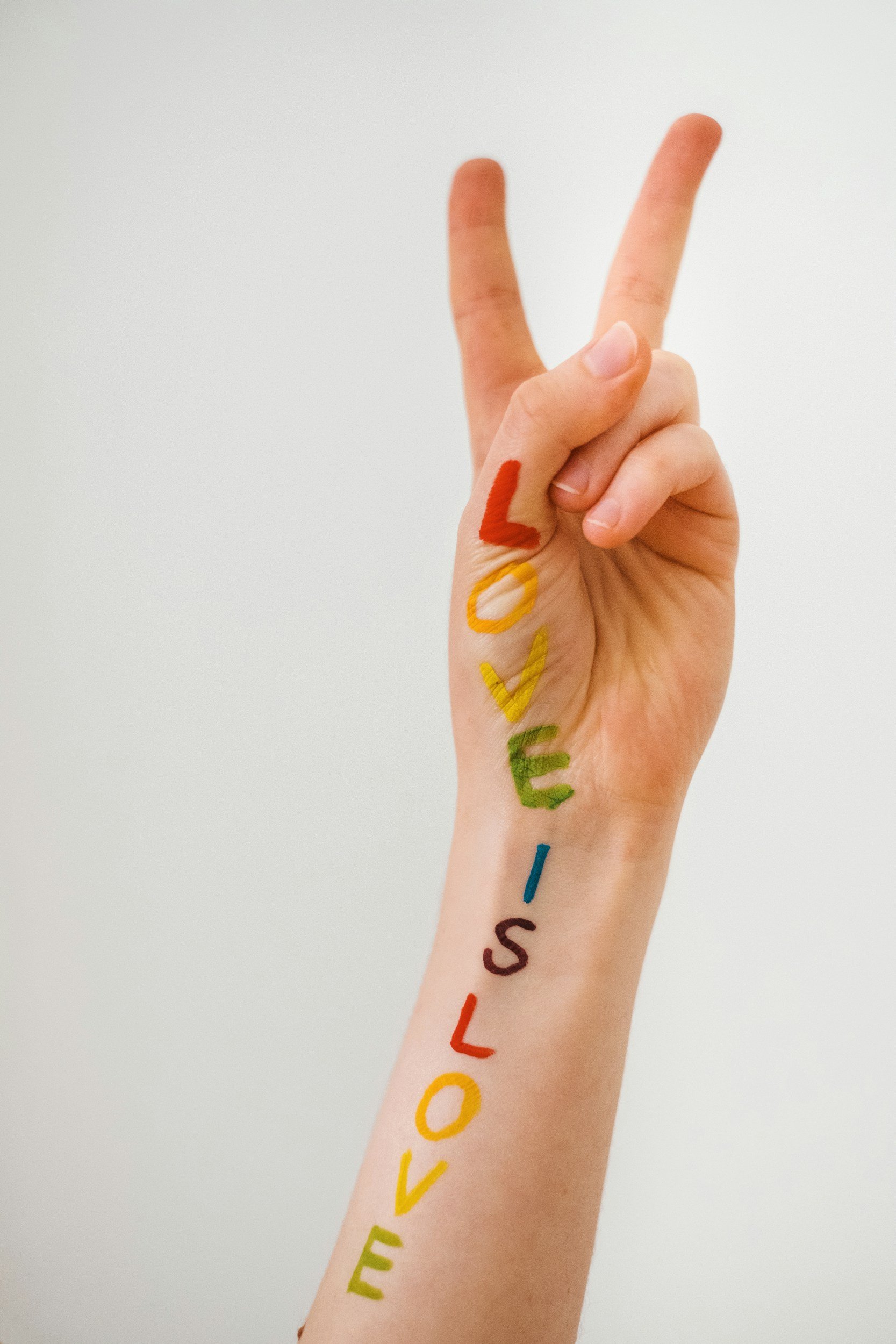 A hand with the word "LOVE" painted on it in rainbow colors, with fingers making a peace sign against a white background.