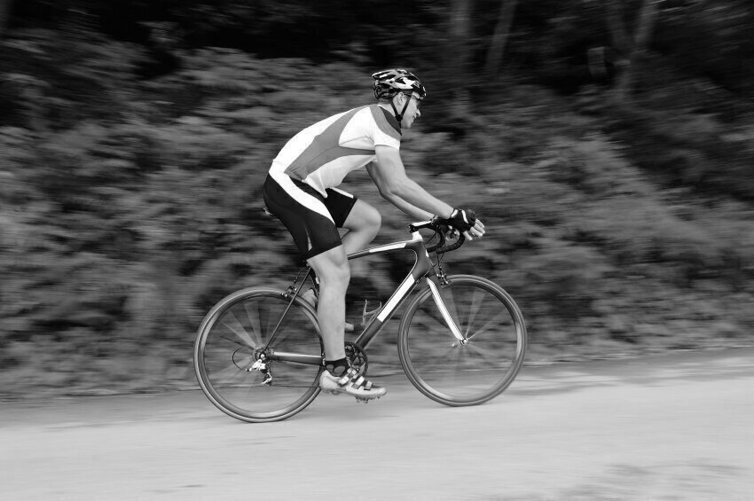 A man riding a bicycle on a paved path with a forest in the background.