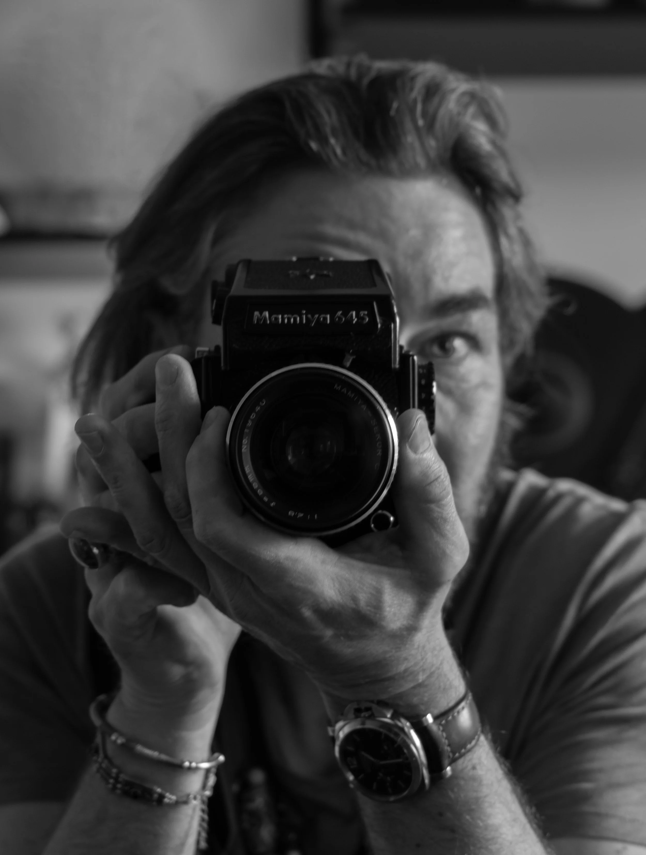 Portrait en noir et blanc d’un photographe tenant un appareil photo reflex devant son visage.