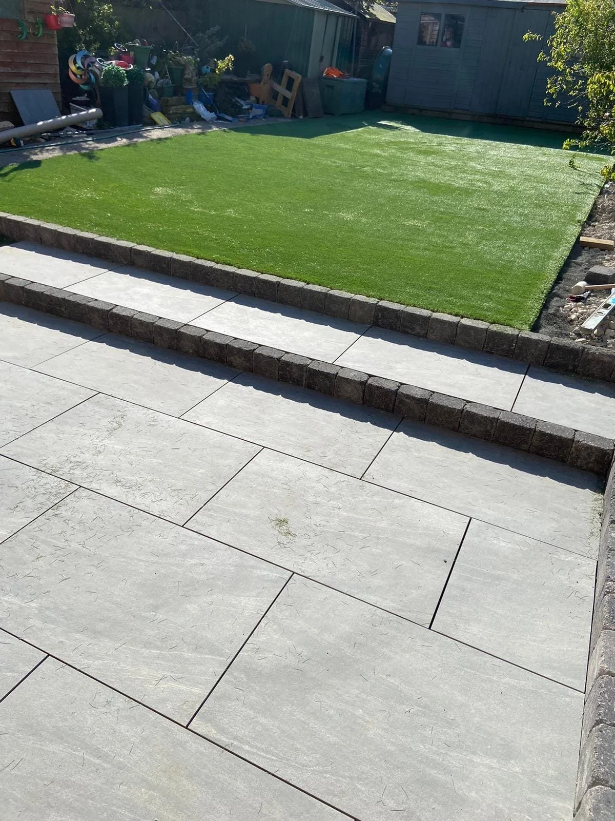 Grey porcelain patio with steps up to artificial lawn