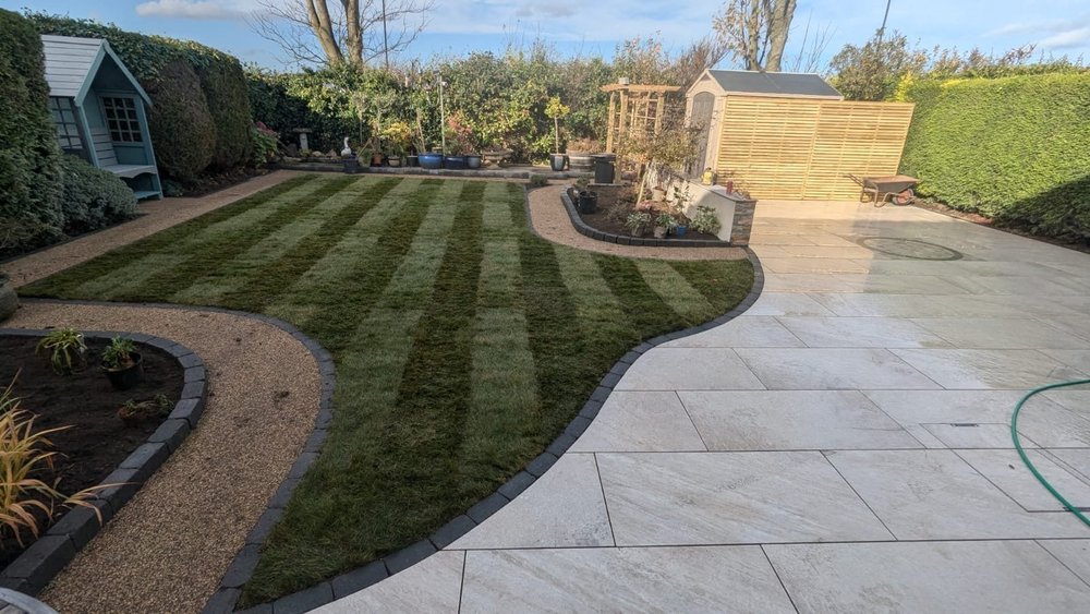 Striped lawn, curved resin path and porcelain patio