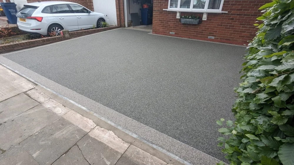 New silver-grey resin-bound driveway with slab edging in front of a brick house