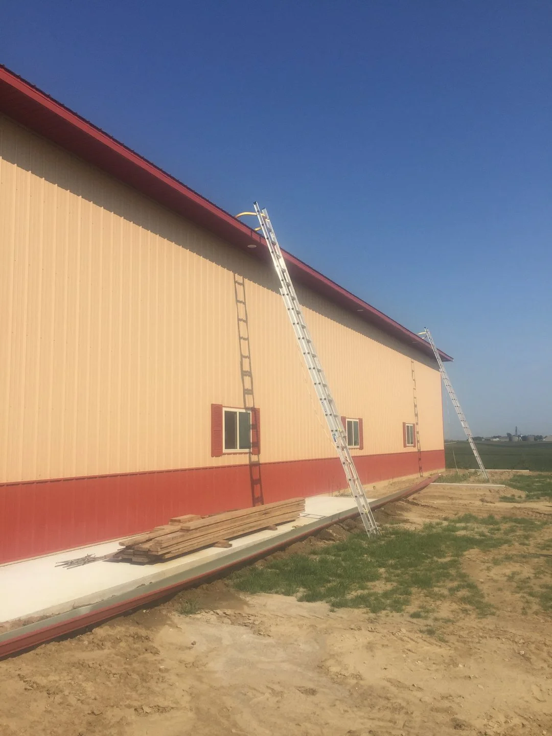 Steel pole building with red trim and ladders during a gutter install