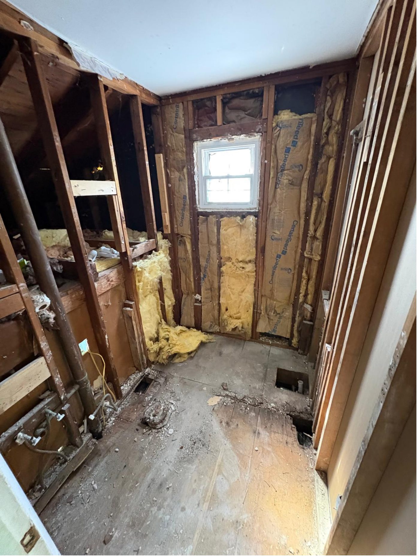 Room under renovation with exposed wooden framing, insulation, and a small window.