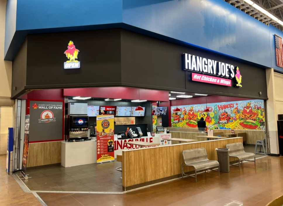 Hangry Joe's fast food restaurant in a shopping center, offering hot chicken and wings, with a colorful mural and seating area.