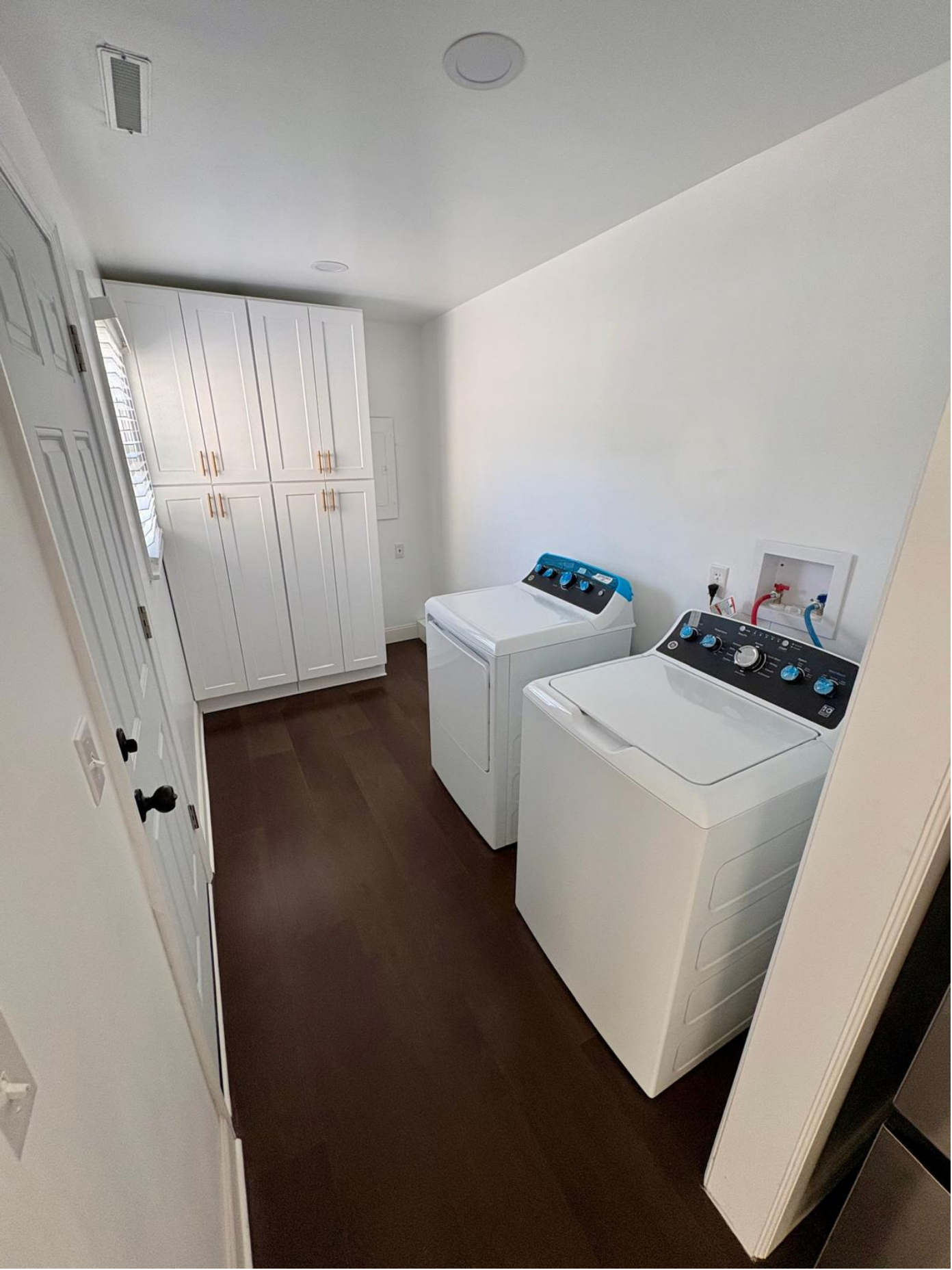 A laundry room with white cabinets, a washing machine, and a dryer on a hardwood floor.