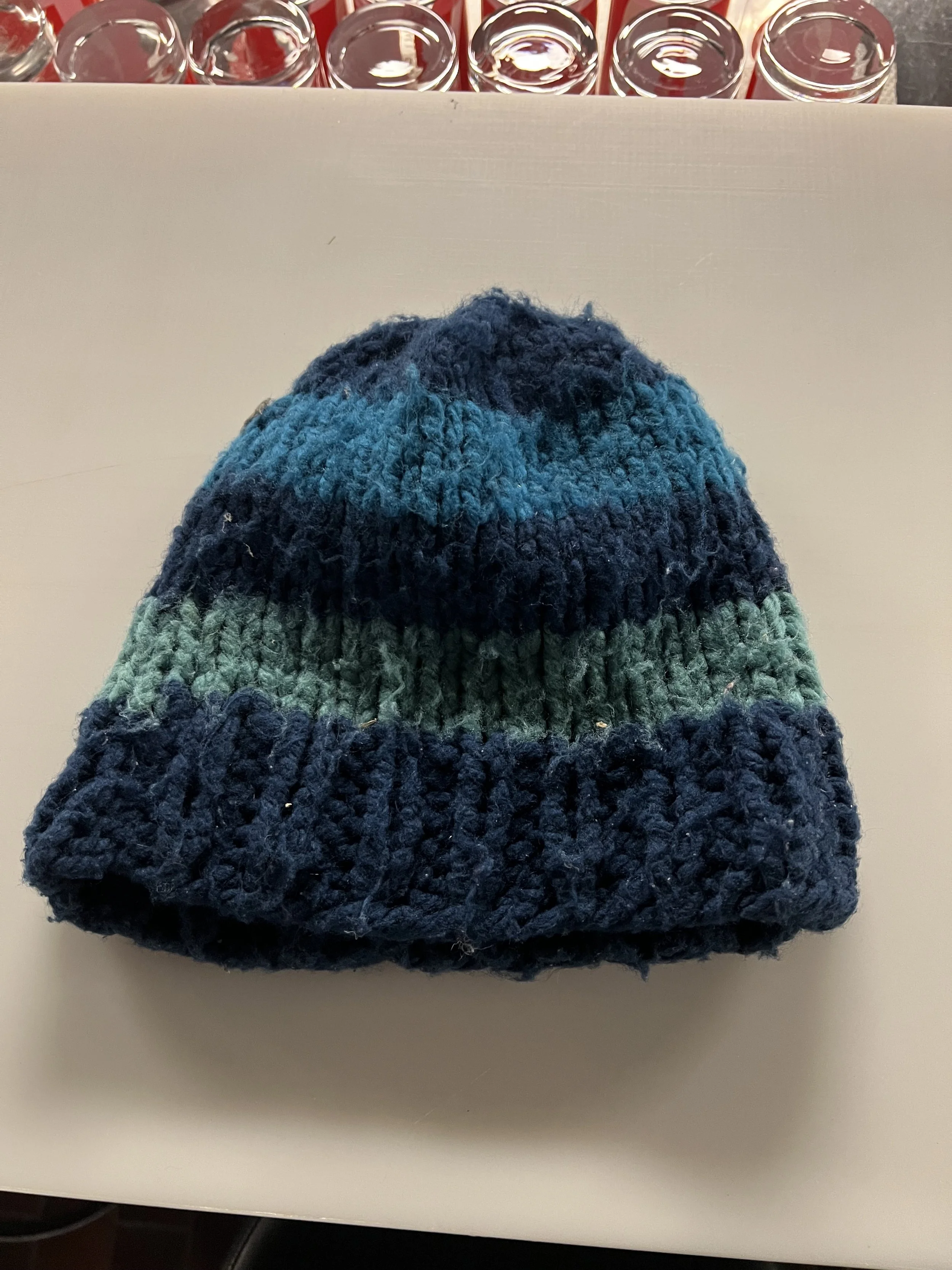 Ein gestreifter, winterlicher Wollhut mit blauen und grünen Farben auf einer weißen Oberfläche.