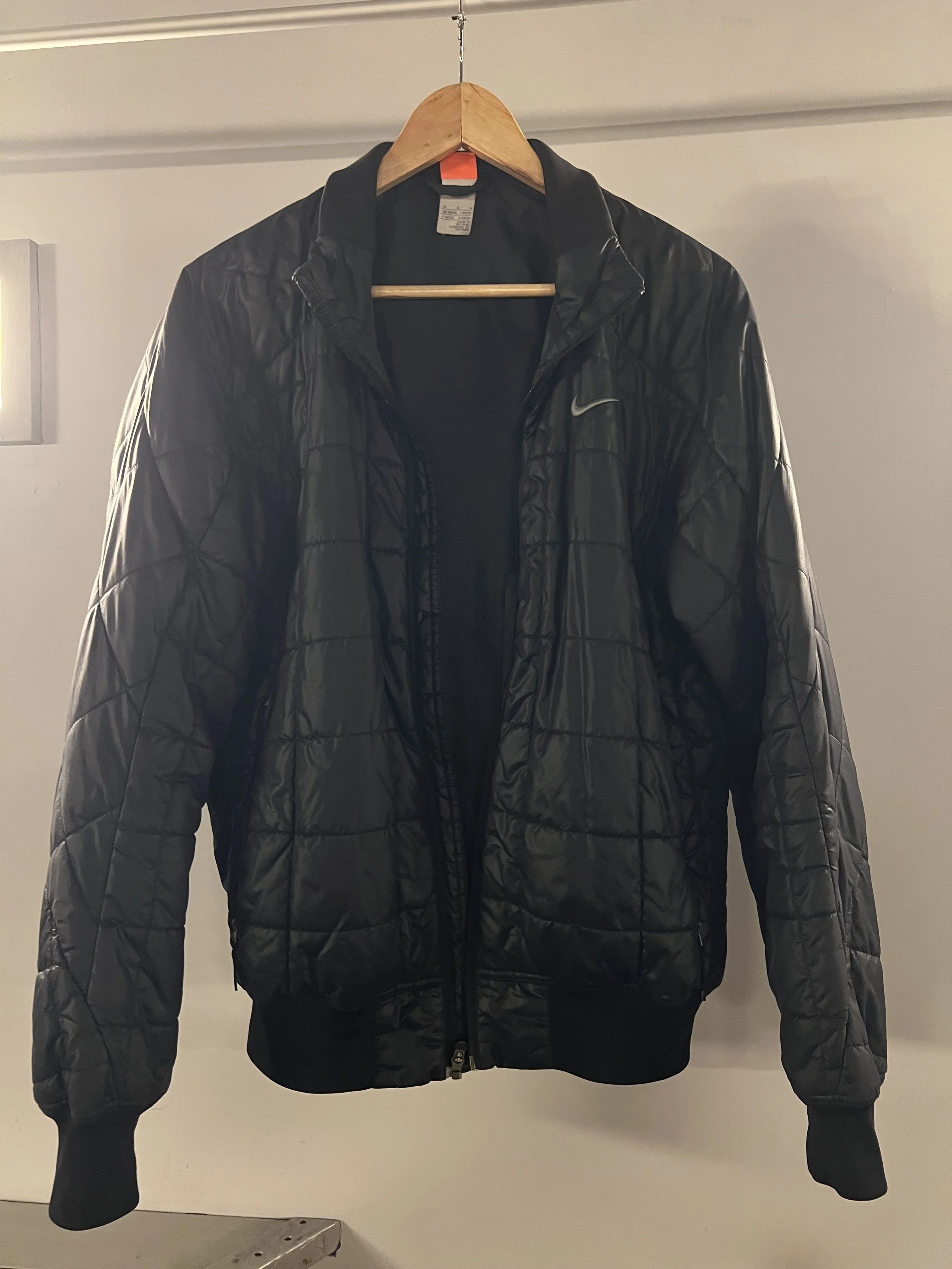 Schwarze Nike Jacke hängt an einem Holzhaken an der Decke.