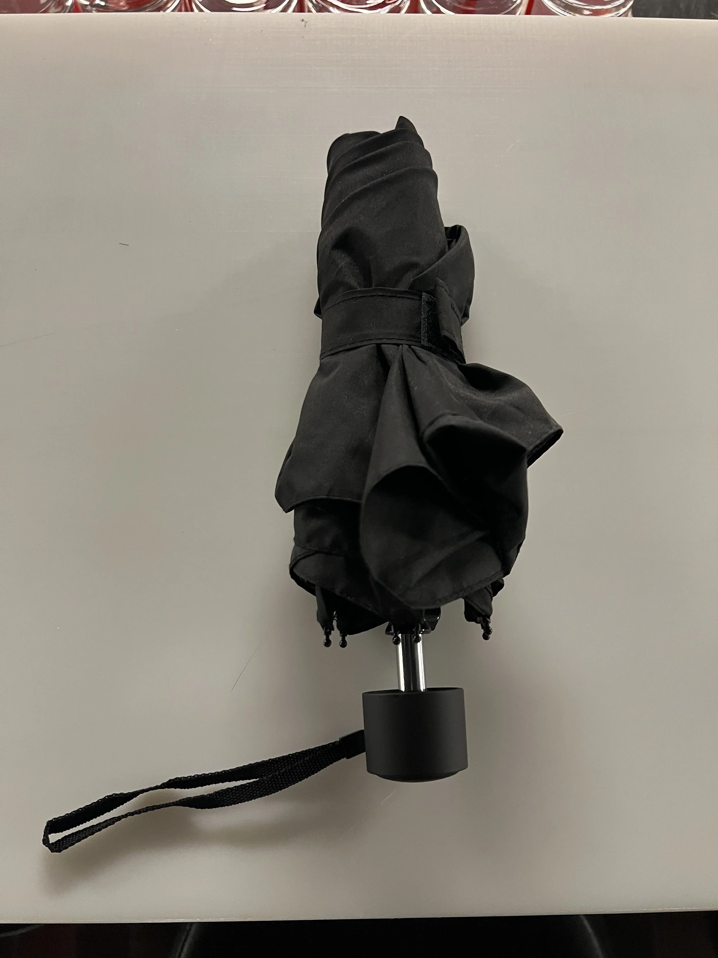 Ein schwarzer Drahtkamera-Objektiv mit schwarzer Tasche und Tragegurt, auf weißem Tisch